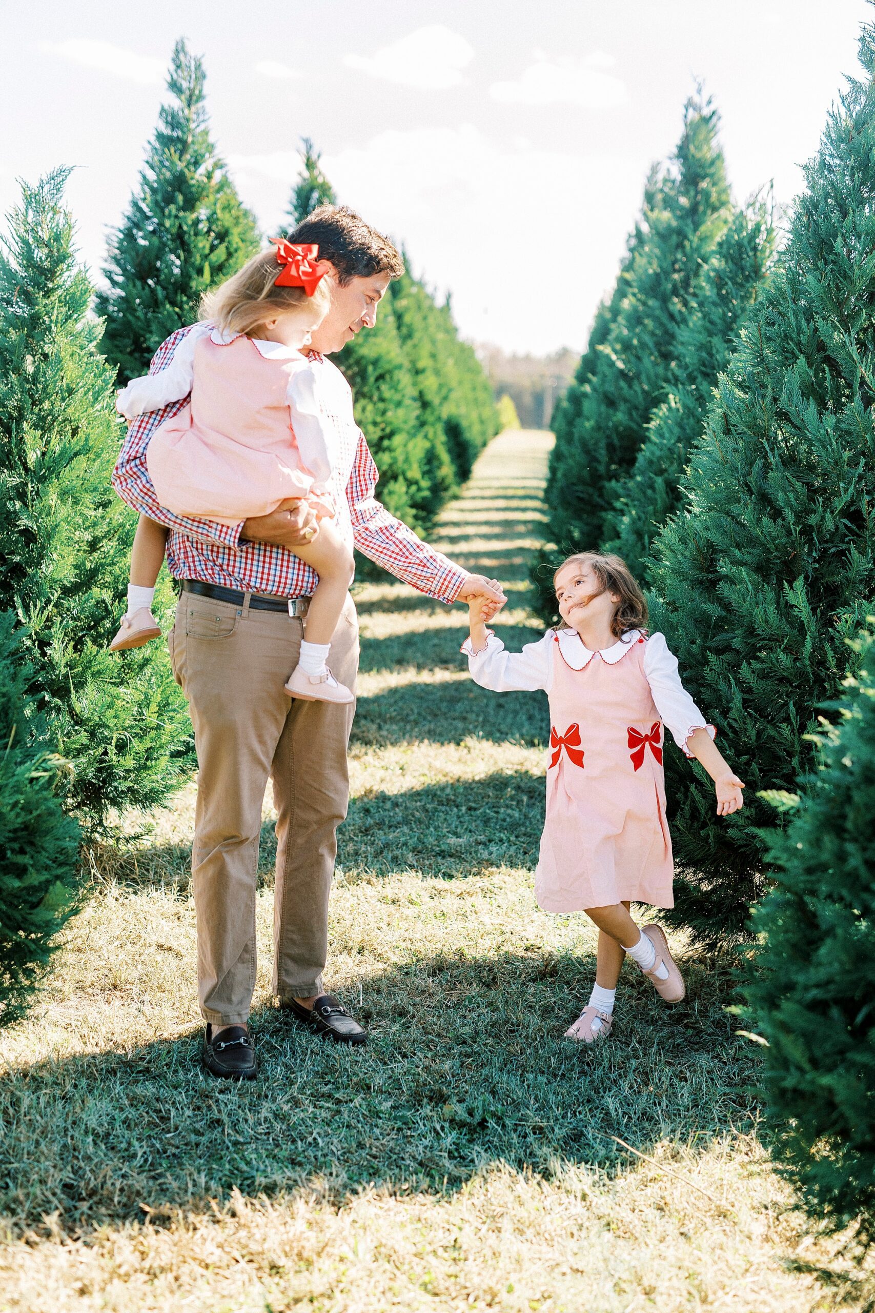 dad walks with two daughters during mini sessions at Penland Christmas Tree Farm