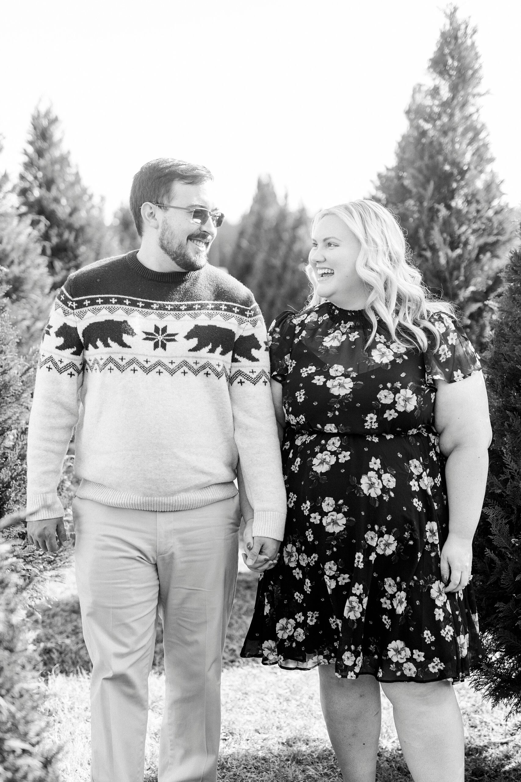 engaged couple holds hands between Christmas trees during holiday mini sessions