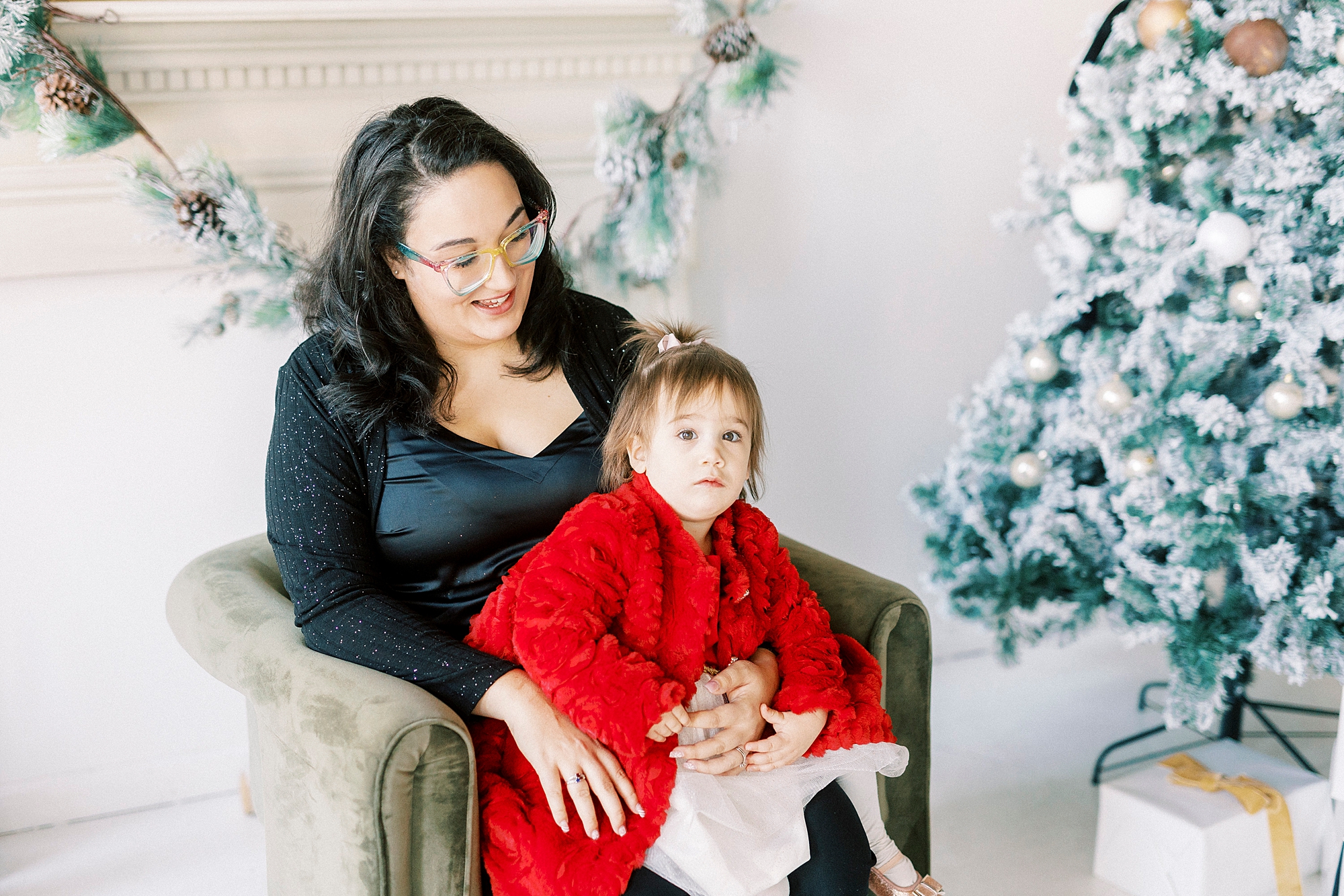 mom sits in green dress with daughter in red dress during holiday portraits 