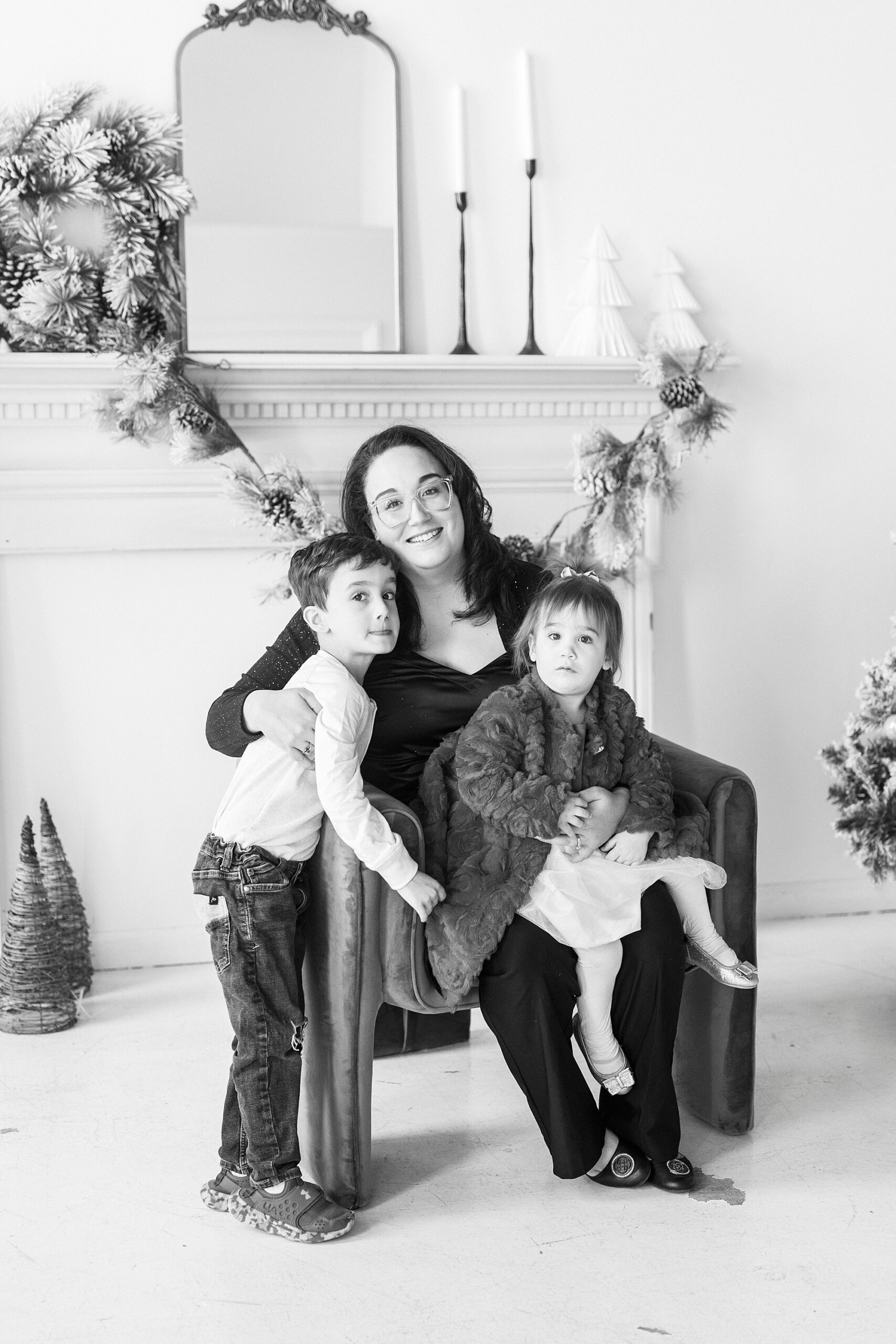 mom hugs two children on her lap in front of Christmas Tree during studio portraits in Concord NC 