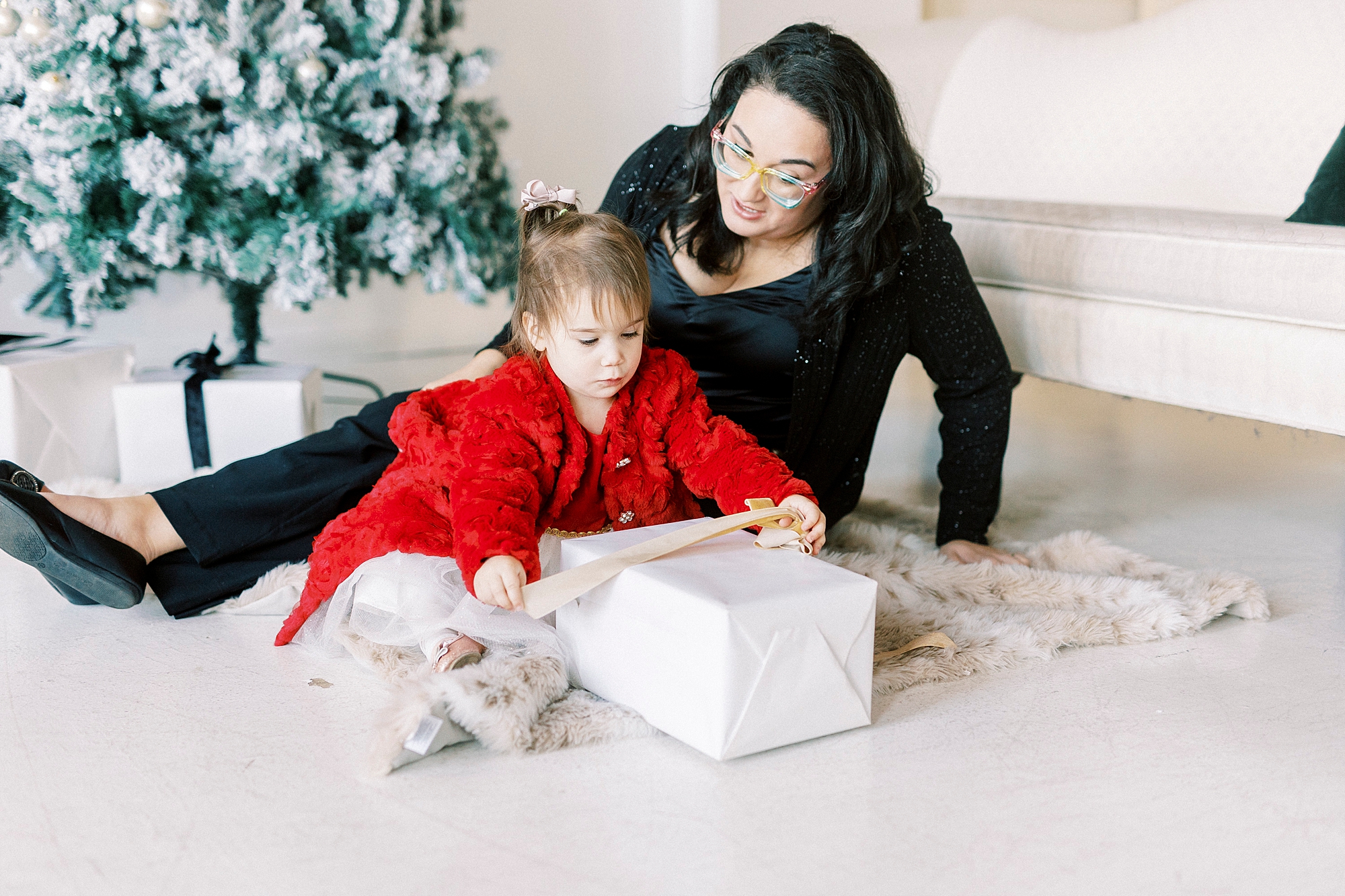 mom sits on ground while daughter opens gift during portraits in Downtown Concord studio