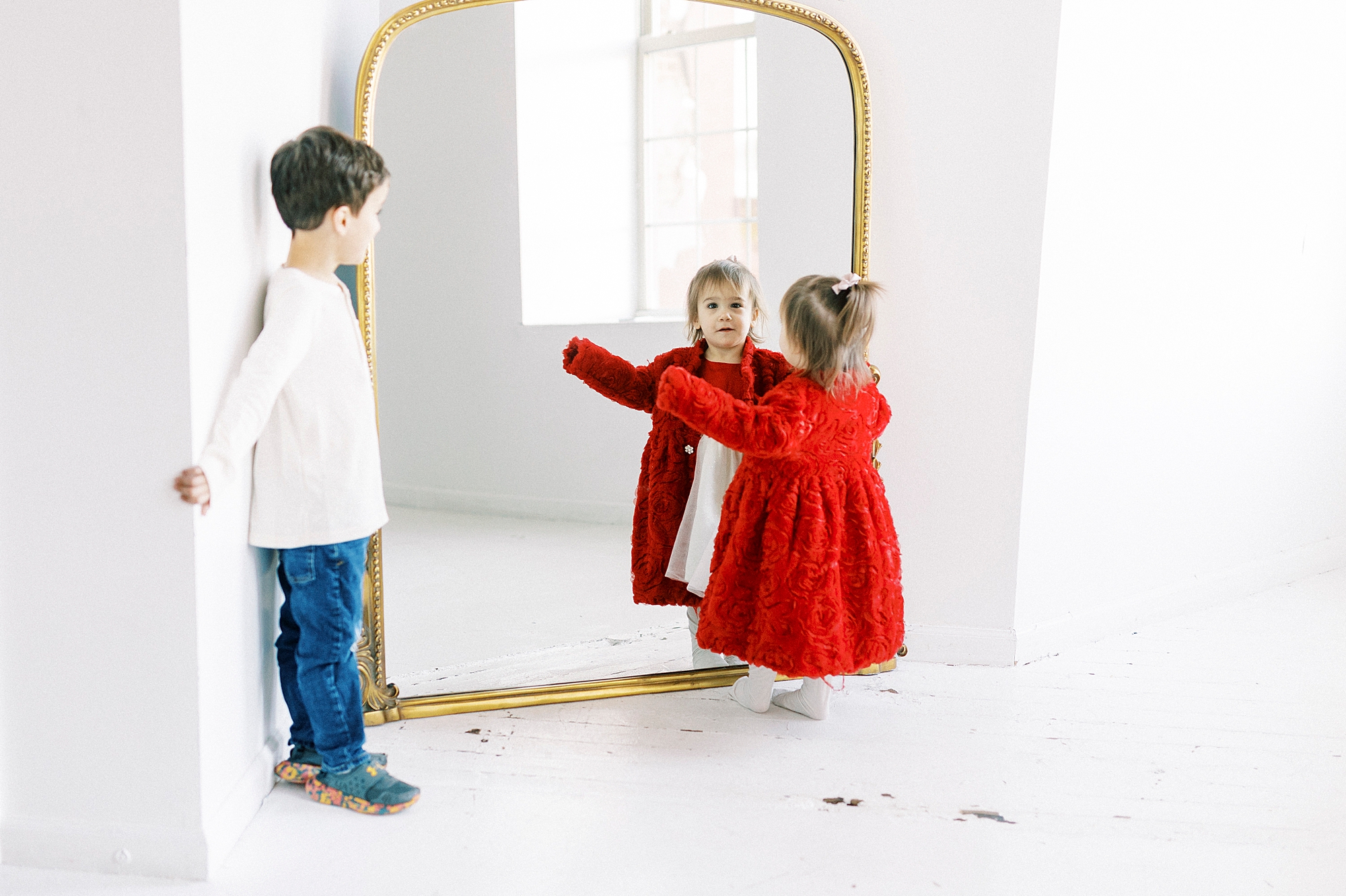 little girl in red dress stands in front of gold mirror in studio