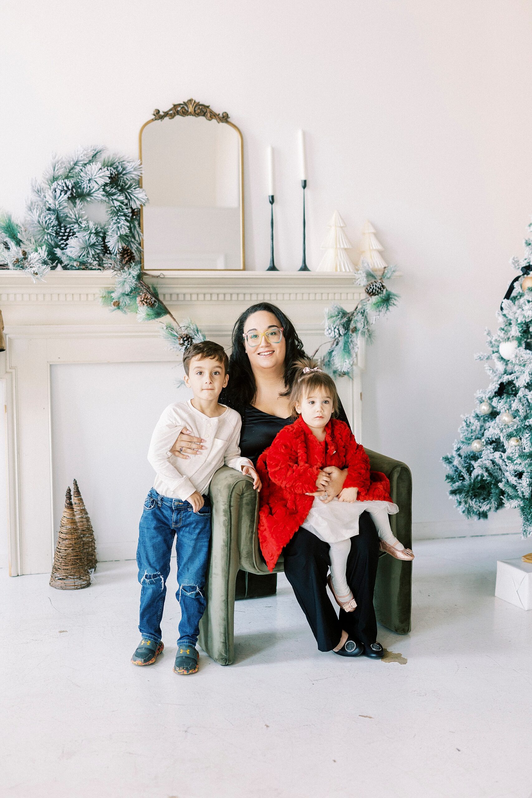 mom sits with children in front of tree and mantel during Christmas portraits in Downtown Concord studio