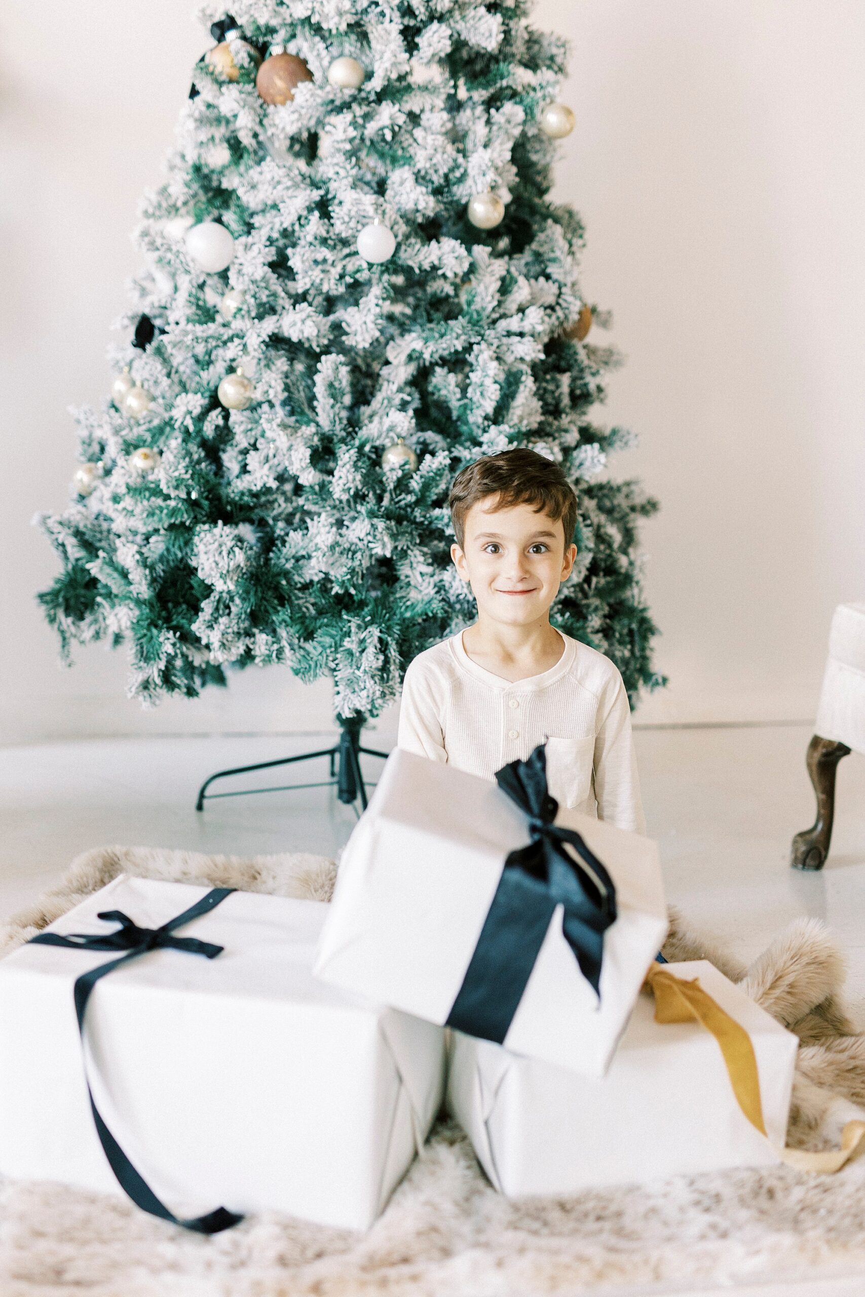son holds presents in front of Christmas tree during portraits in Downtown Concord studio