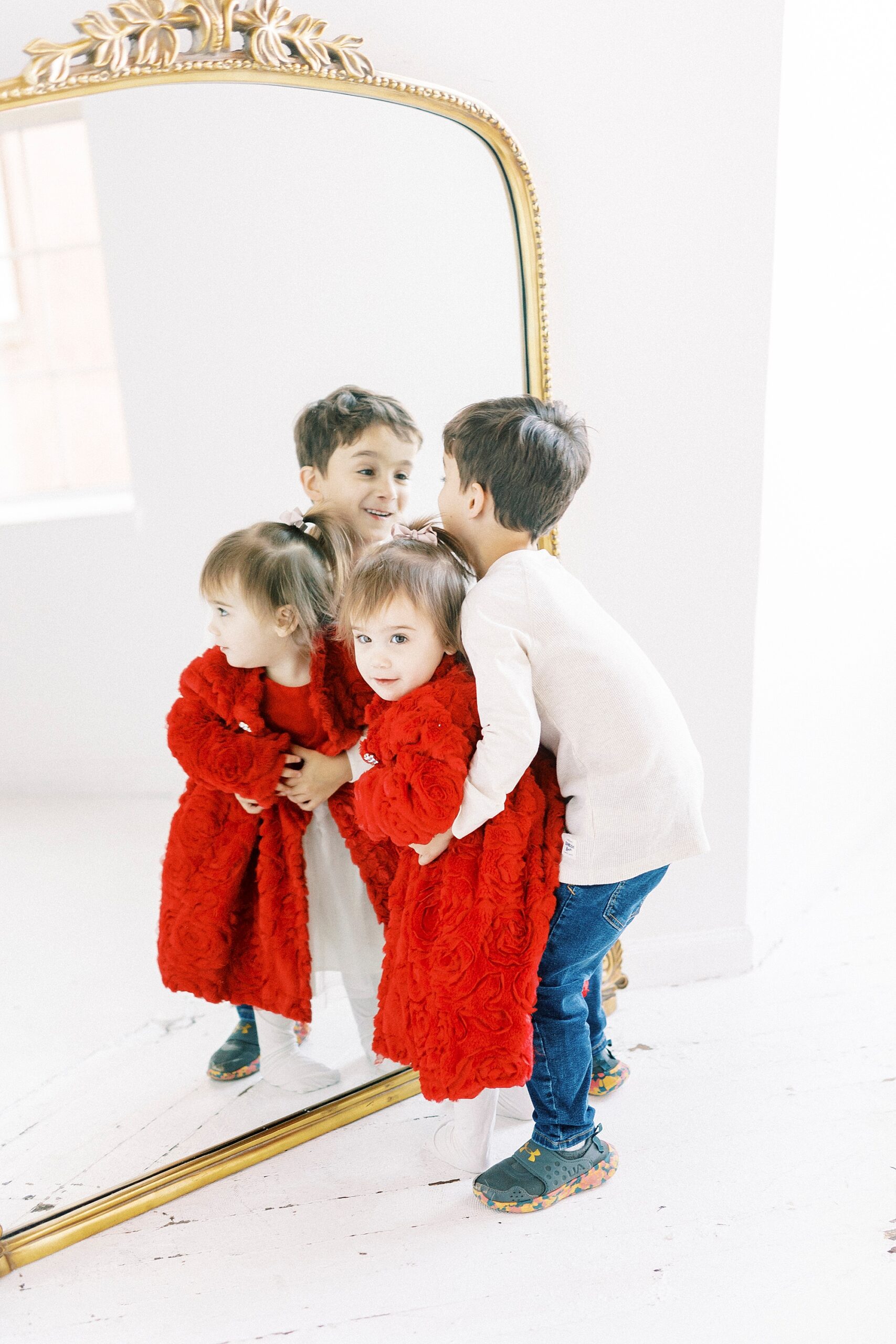 siblings hug in front of mirror during holiday portraits in Concord NC studio
