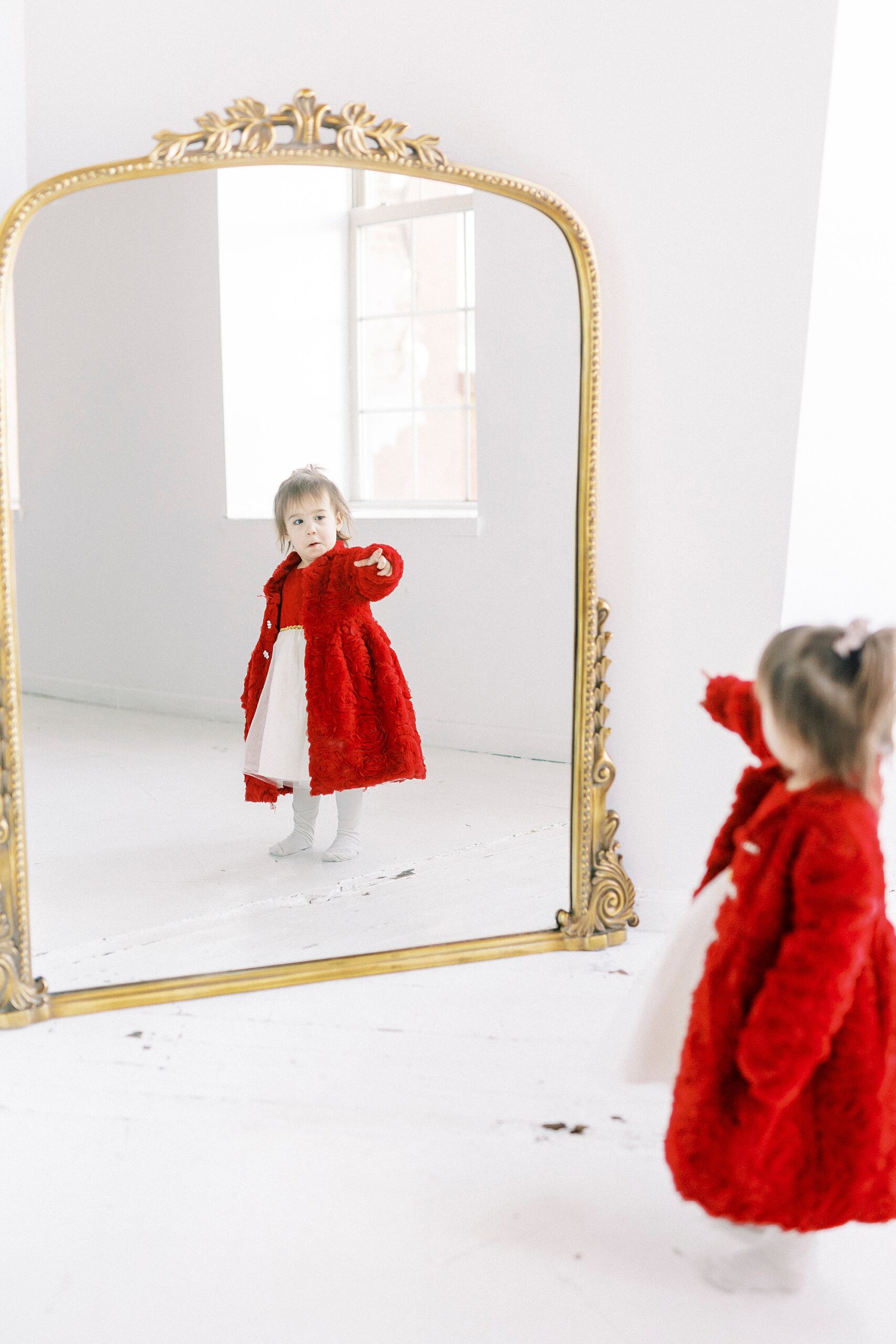 girl in red dress dances in front of mirror during portraits in Concord NC studio