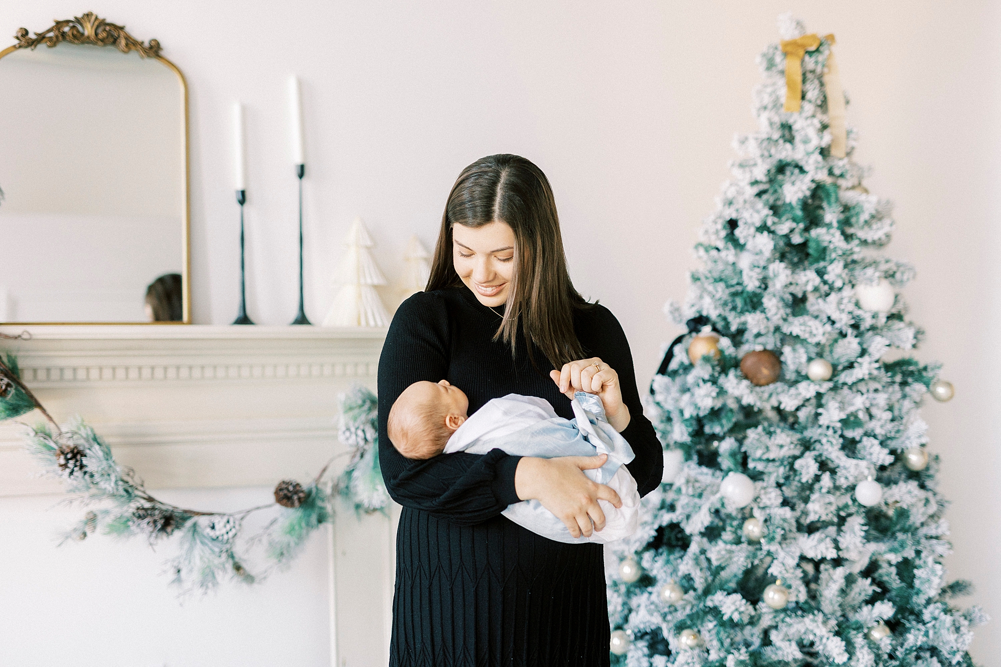 woman hugs baby by decorated mantle during studio Christmas portraits in Downtown Concord