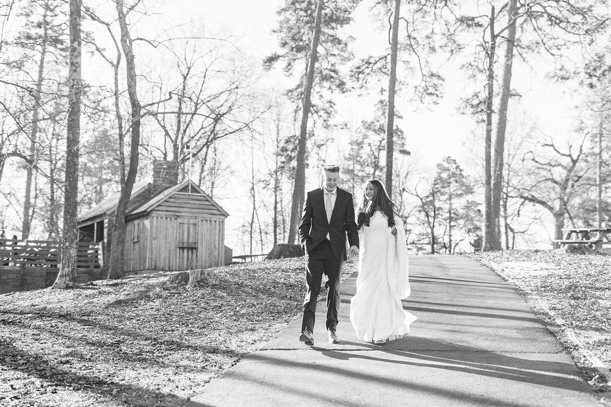newlyweds hold hands walking down hill in front of cabin on Morrow Mountain