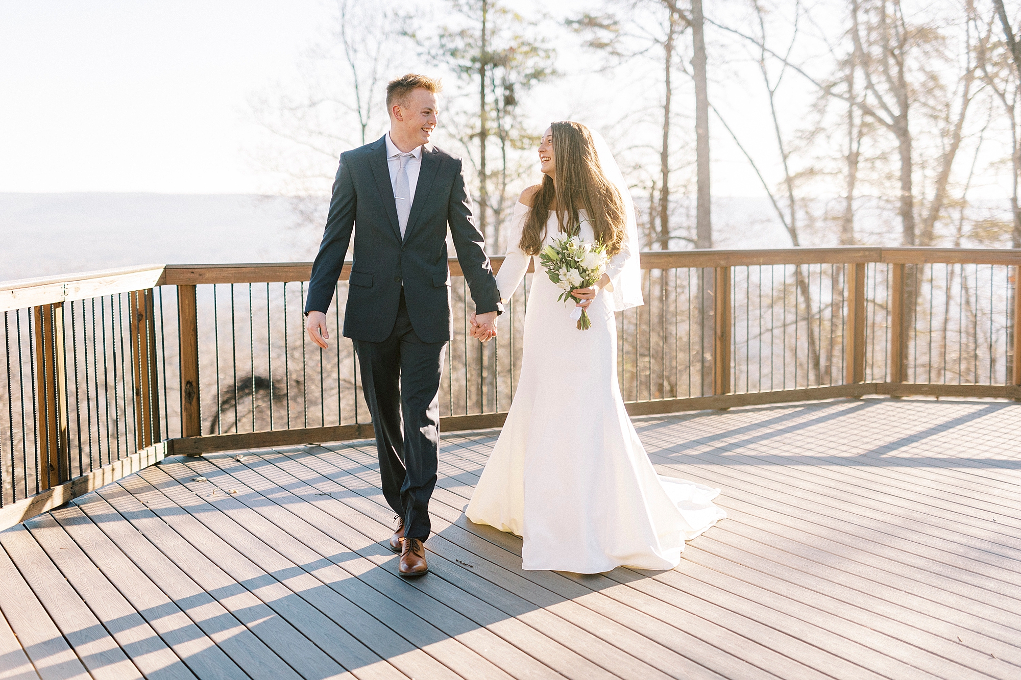 newlyweds hold hands walking across patio at Morrow Mountain
