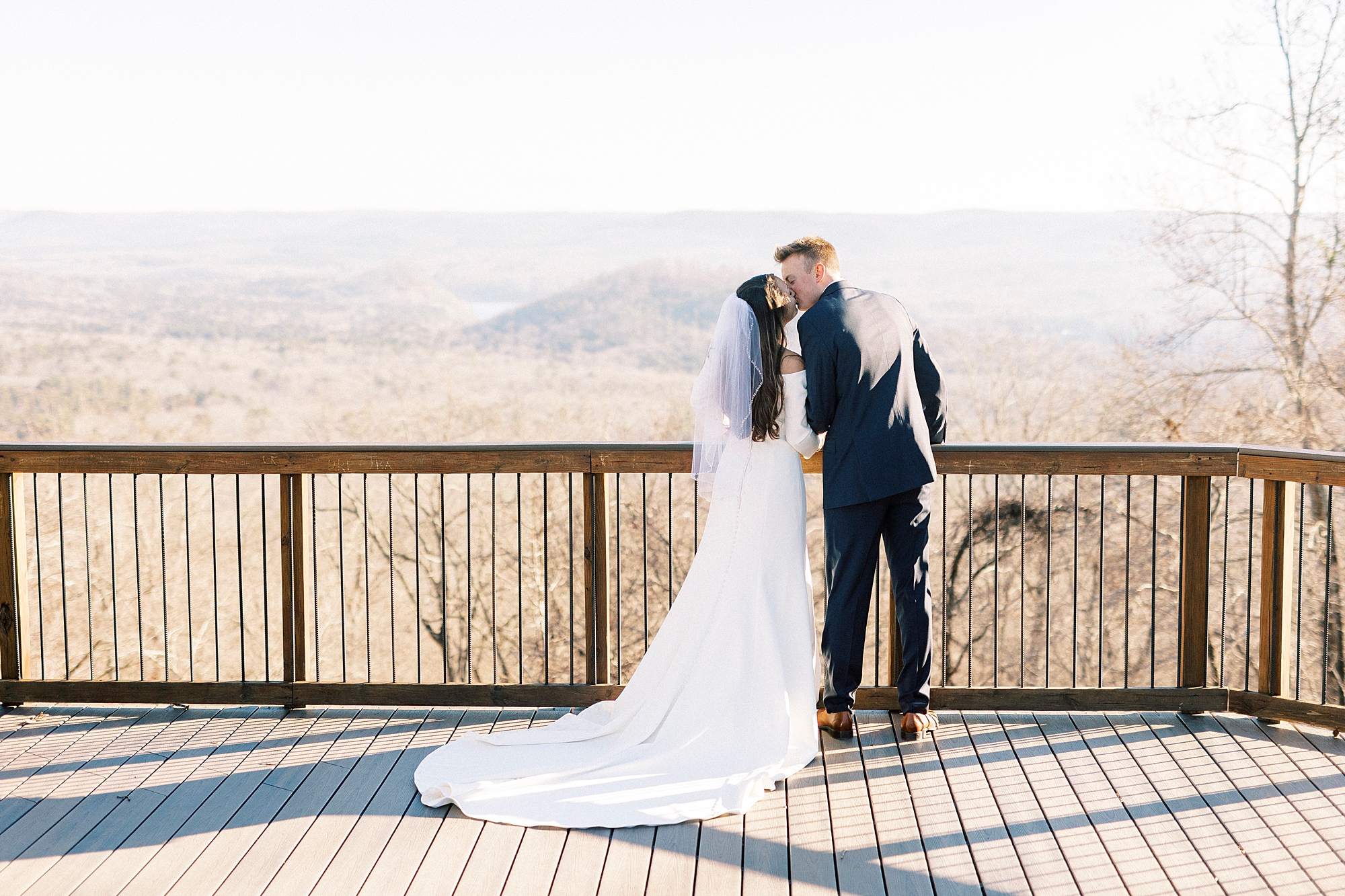 groom leans to kiss bride on patio overlooking Morrow Mountain