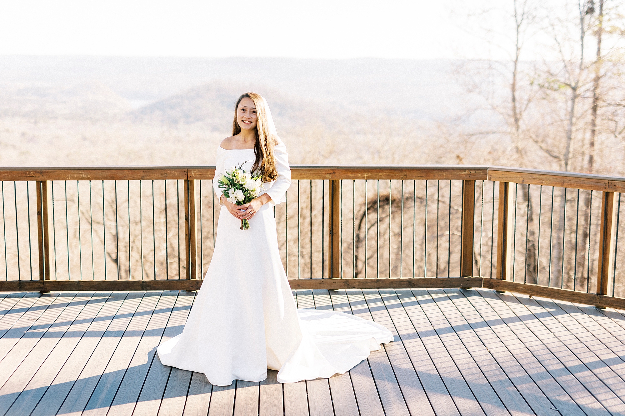bride stands on wooden patio in off-the-shoulder long sleeve gown