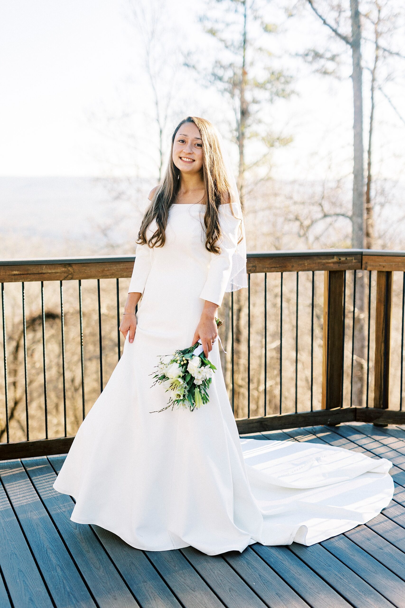bride holds up skirt of wedding gown while holding bouquet of ivory flowers for winter wedding on Morrow Mountain