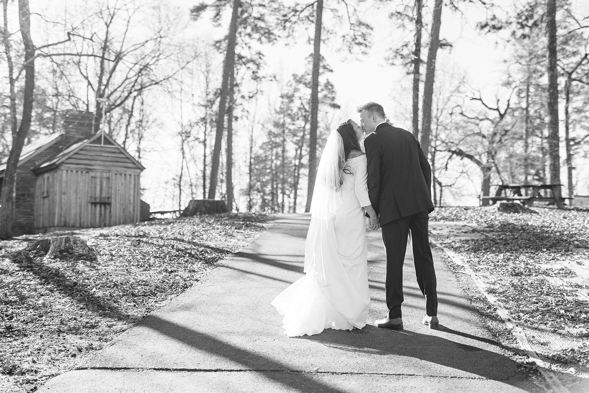 bride leans to kiss groom on walkway leading to cabin at Morrow Mountain