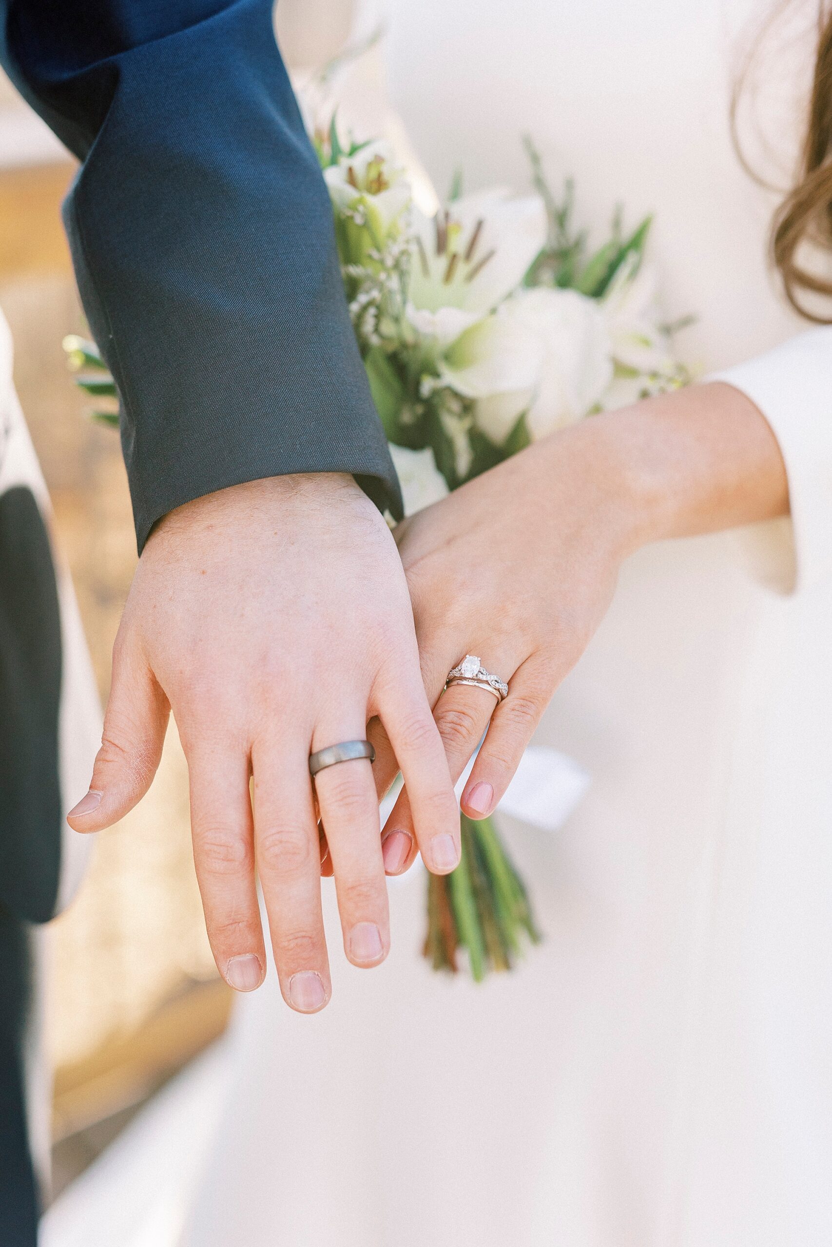bride and groom hold out hands showing off wedding bands 