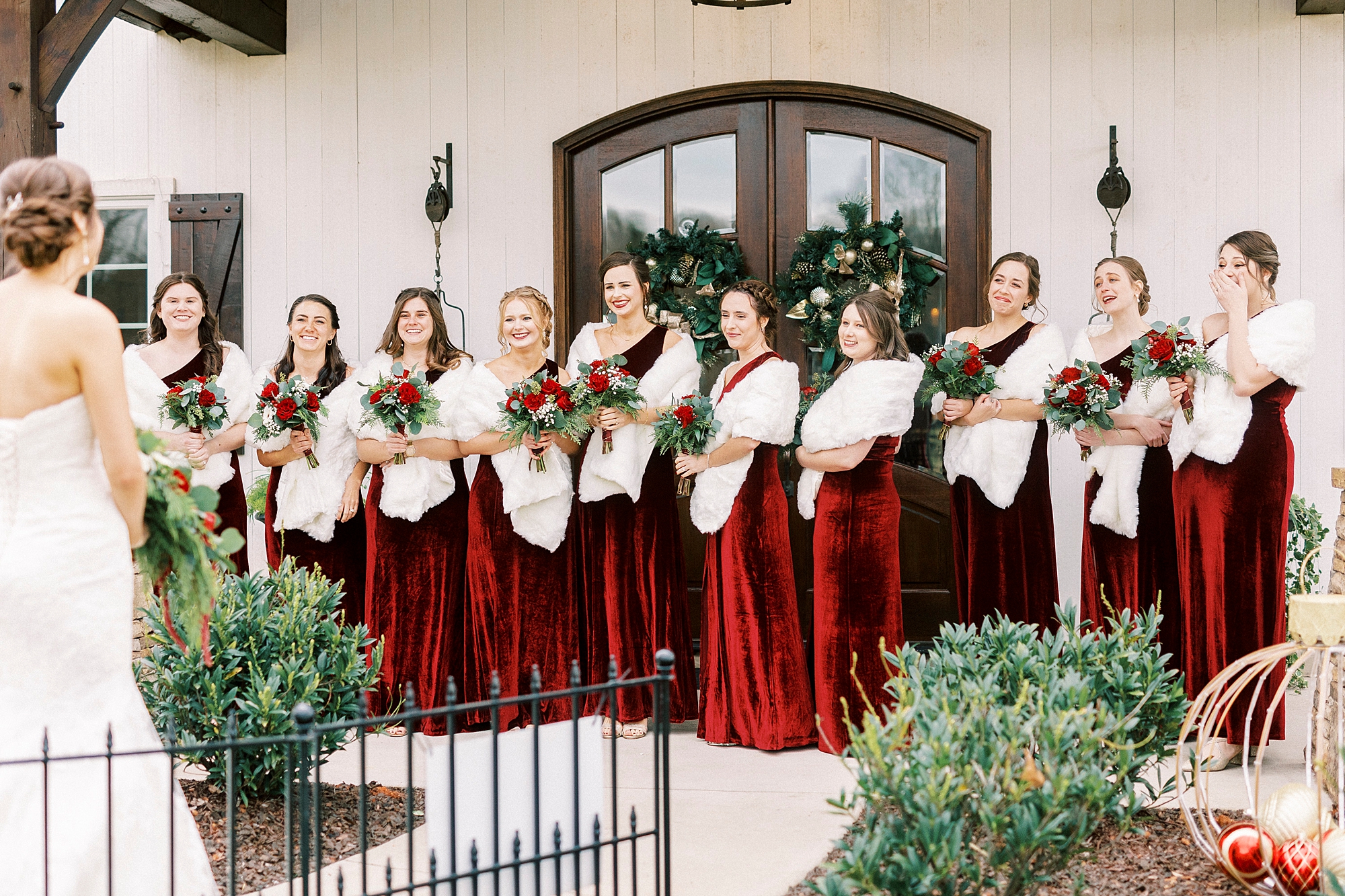 bride stands with bridesmaids in red gowns with white furs for winter Chickadee Hill Farms wedding