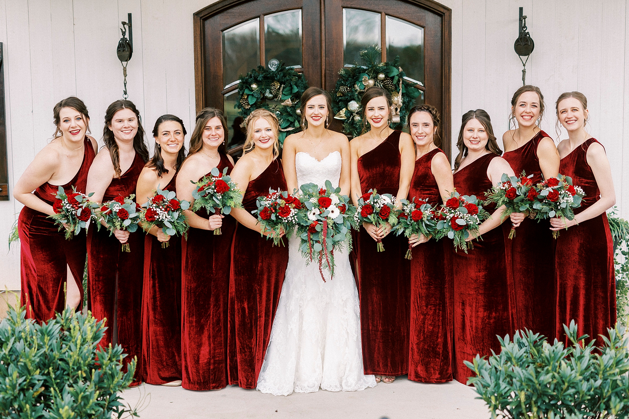 bride poses with bridesmaids in one shoulder burgundy gown before winter Chickadee Hill Farms wedding