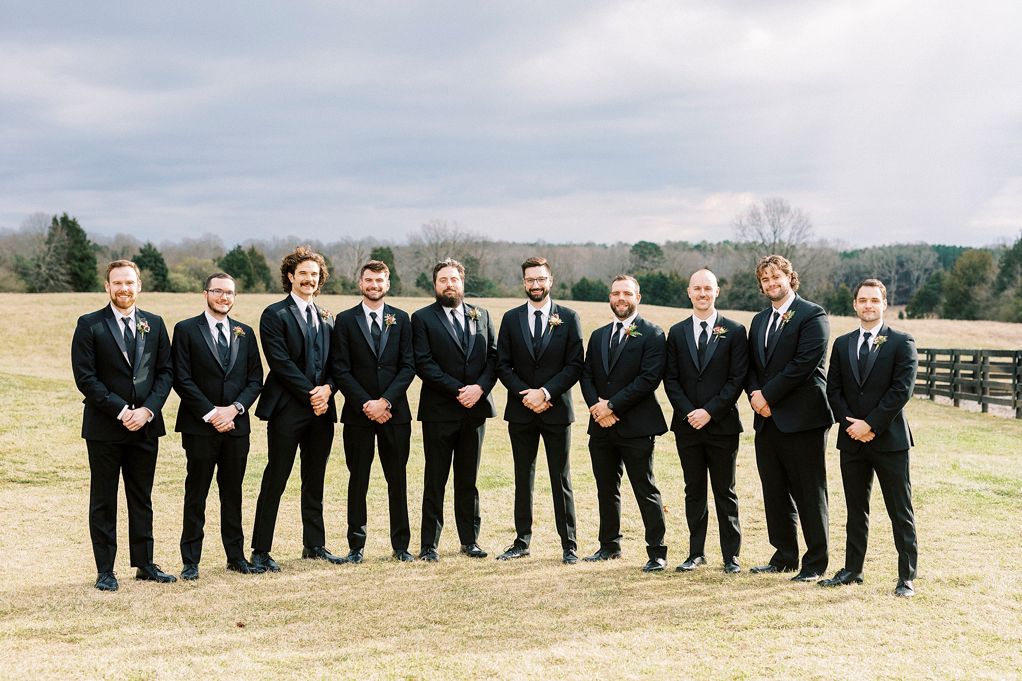 groom and groomsmen stand in a line on the edge of a field at Chickadee Hill Farms