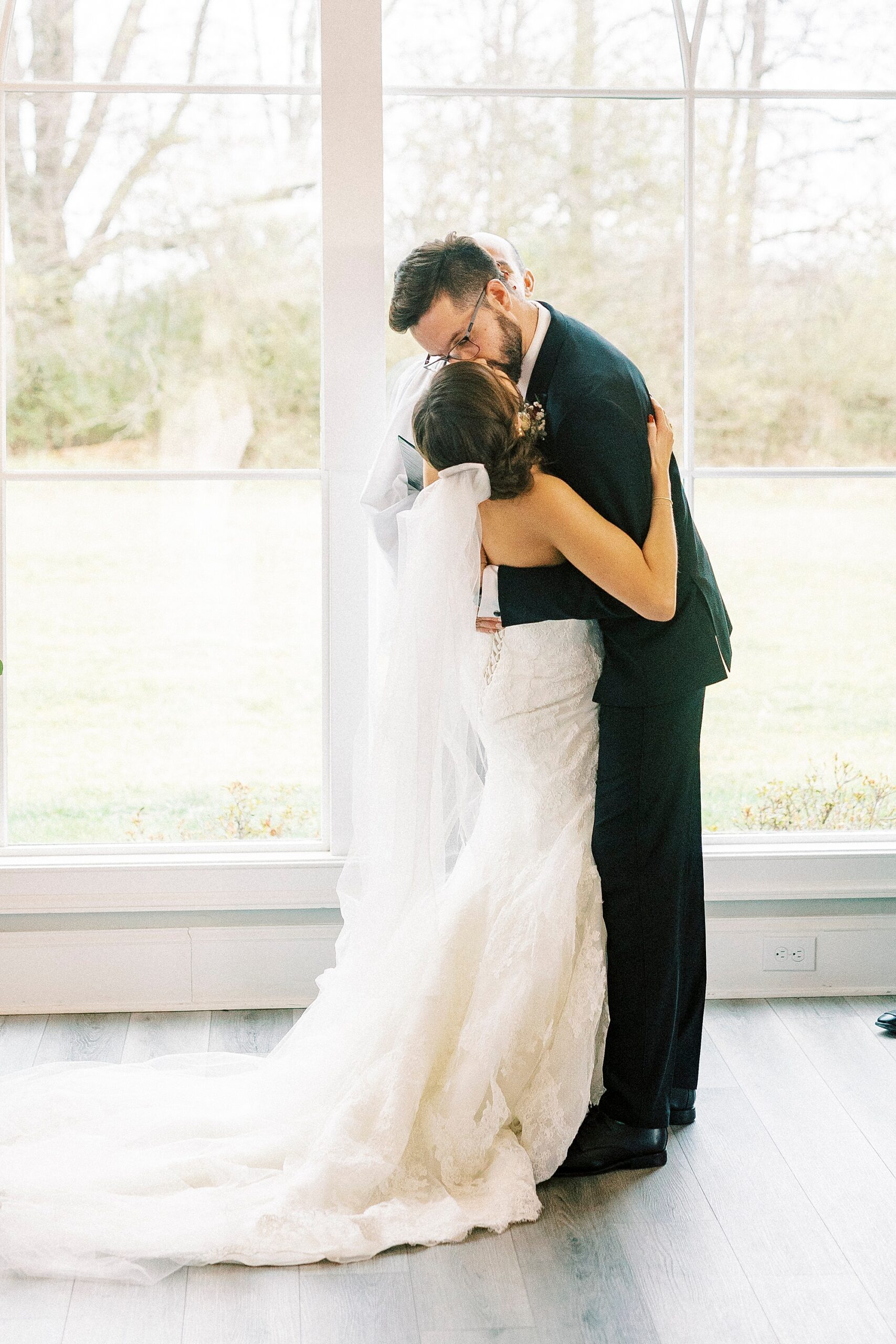 newlyweds kiss by big window for Chickadee Hill Farms wedding ceremony