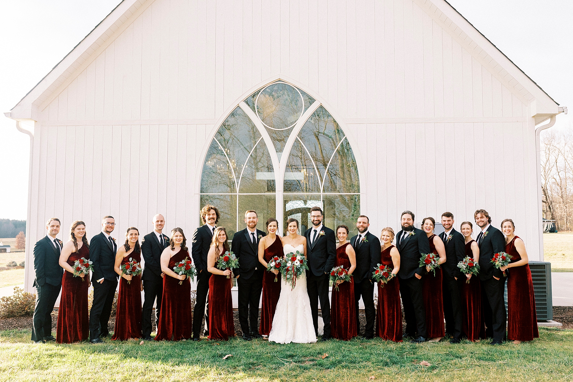bride and groom stand with wedding party in burgundy gowns and black suits 