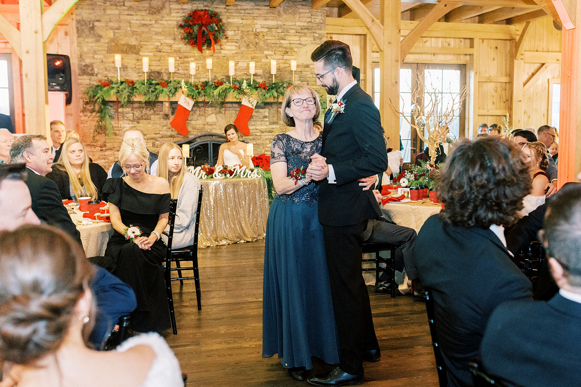 groom dances with mother in blue dress during Christmas wedding at Chickadee Hill Farms