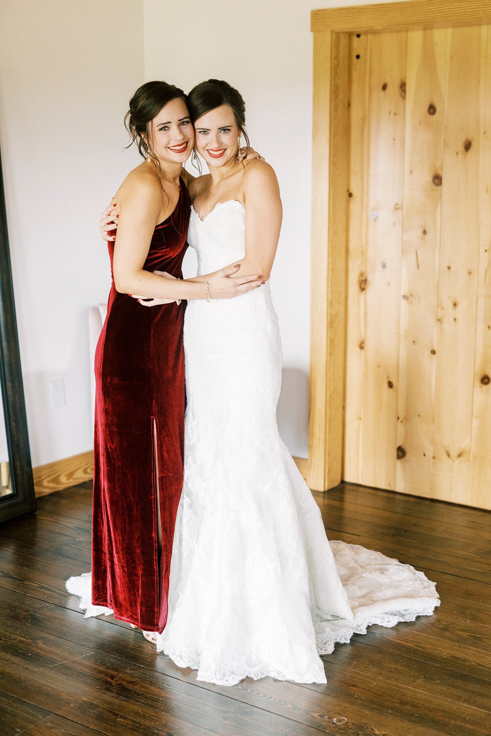 bride hugs bridesmaid in burgundy gown at Chickadee Hill Farms