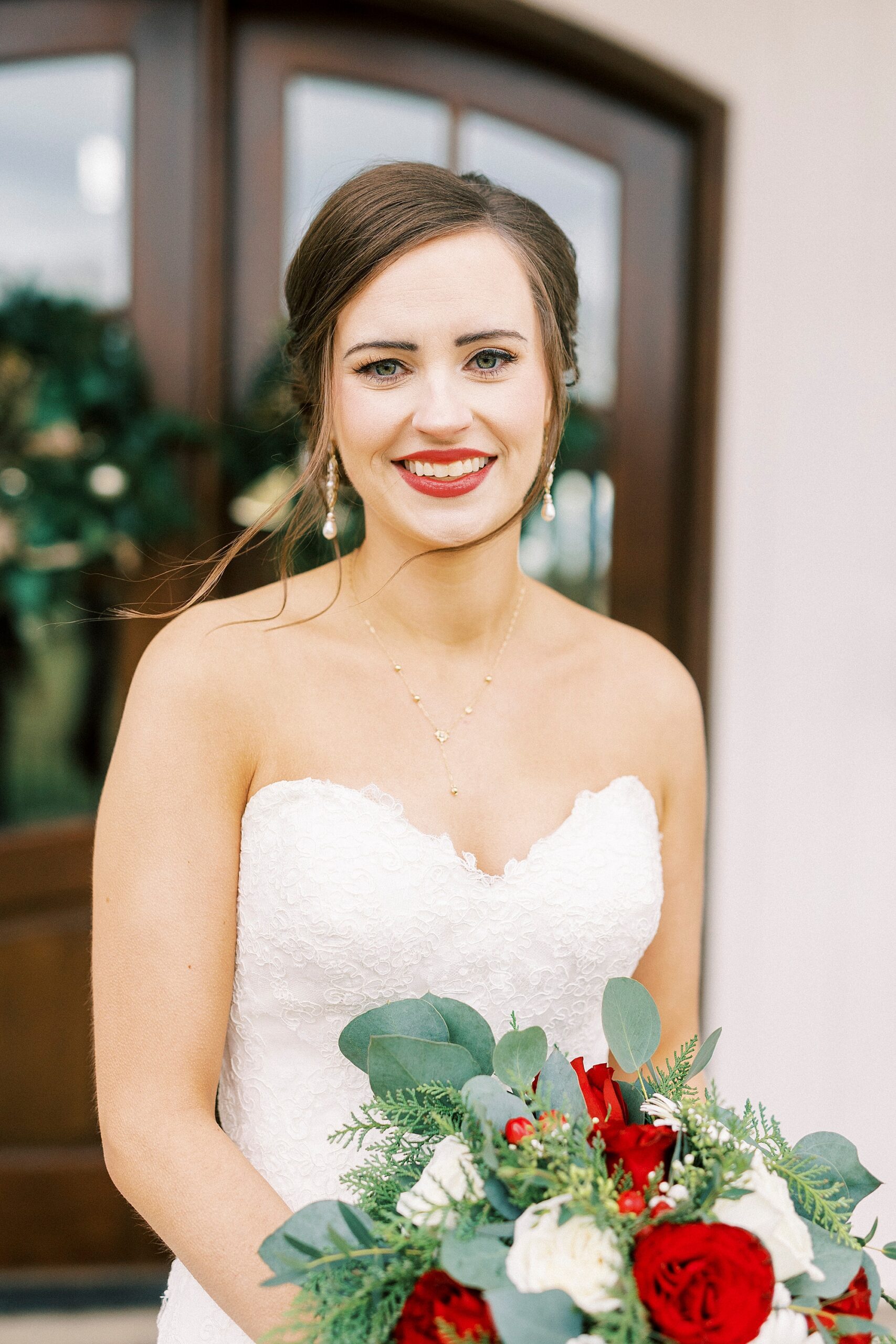 winter bride smiles in strapless gown holding red and white bouquet 