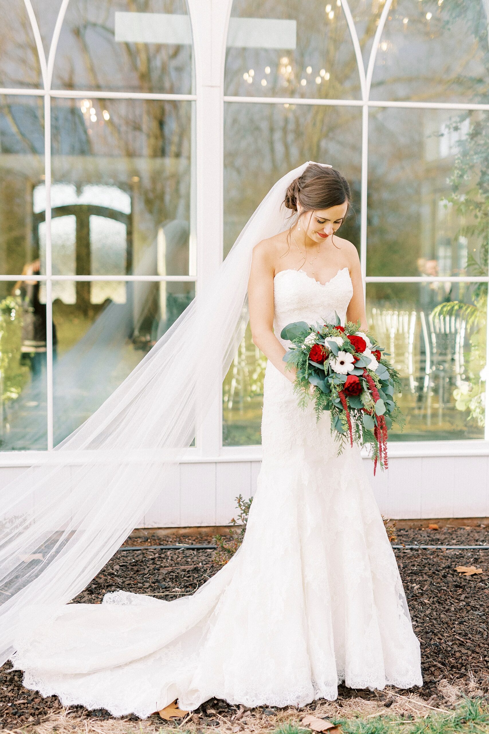 bride in strapless gown holds bouquet of white and red flowers outside Chickadee Hill Farms