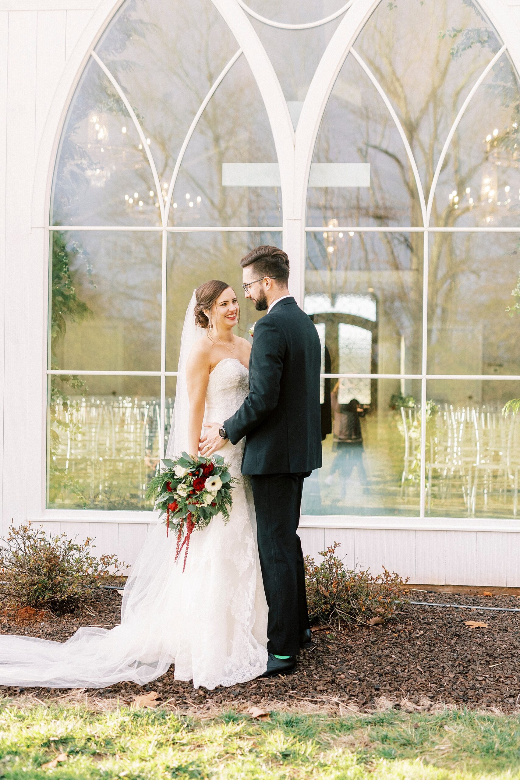 bride and groom hug in front of big white windows at chapel of Chickadee Hill Farms