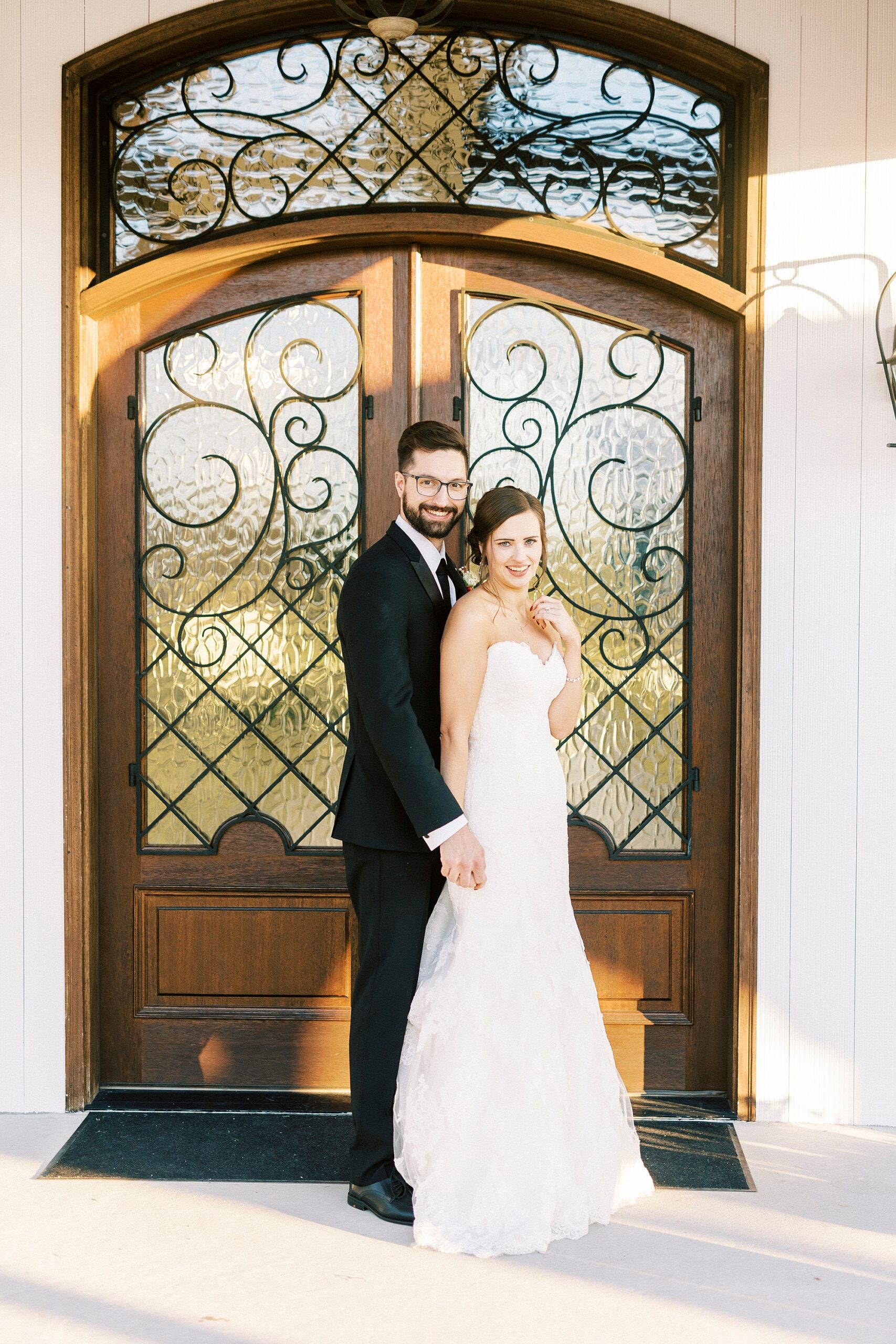 bride and groom hold hands standing front to back in front of wooden doors at Chickadee Hill Farms