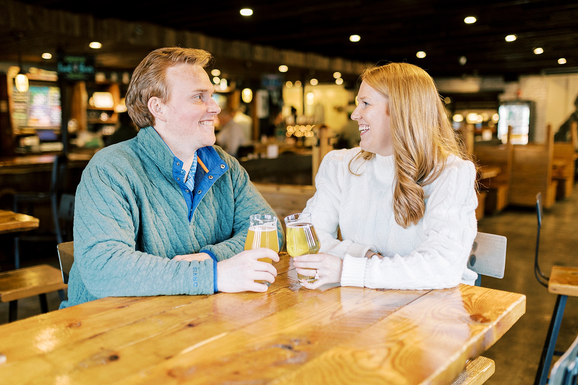 engaged couple sits holding pints of beer at Legion Brewing in Charlotte NC