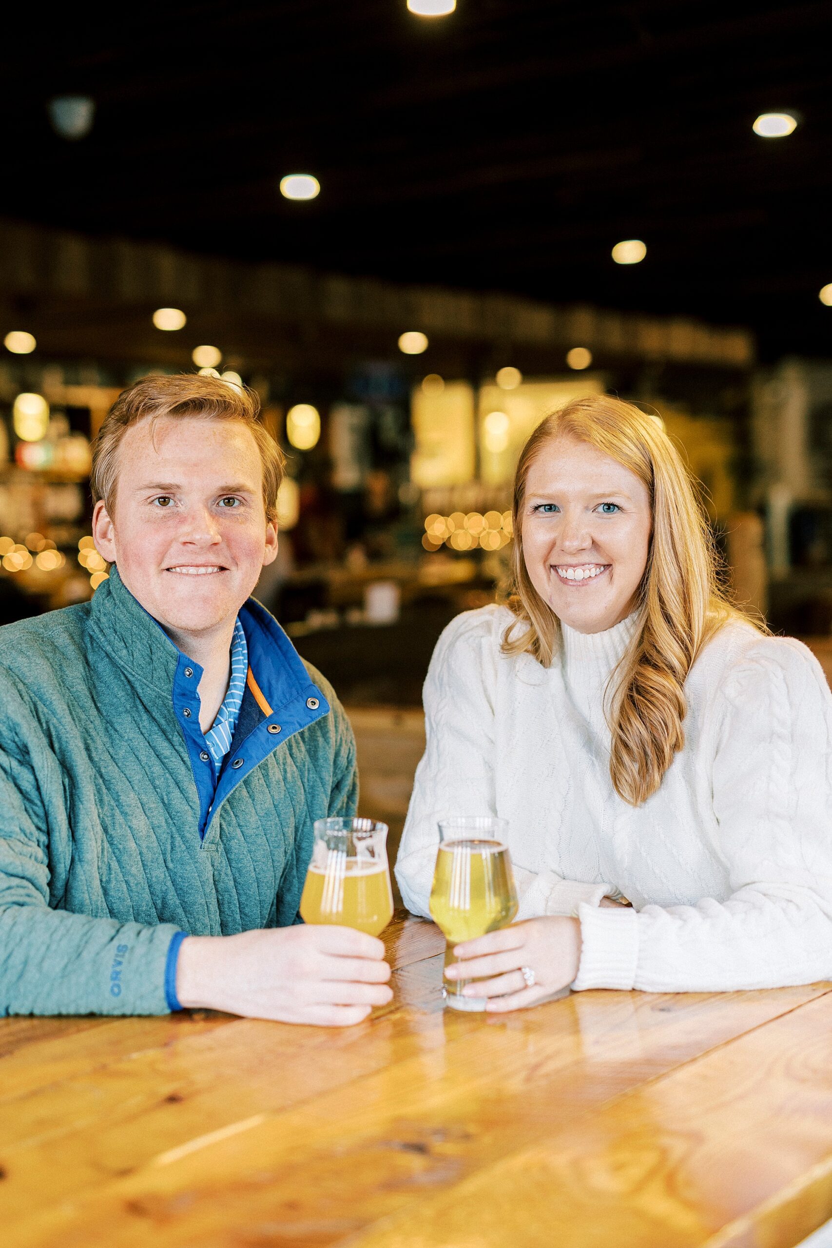 engaged couple holds onto glasses of beer at Legion Brewing in Charlotte NC
