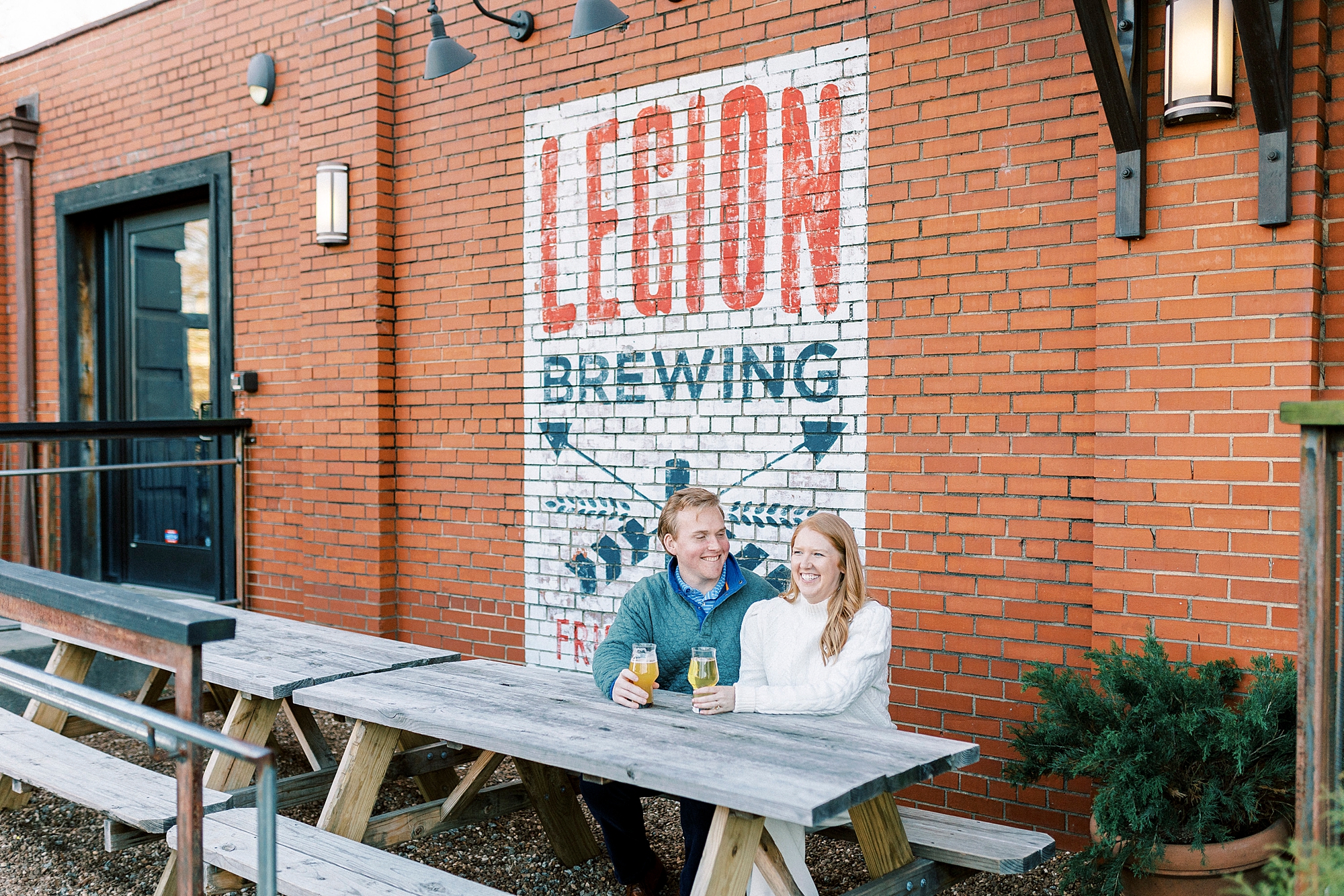 engaged couple talks sitting at picnic table at Legion Brewing in Charlotte NC