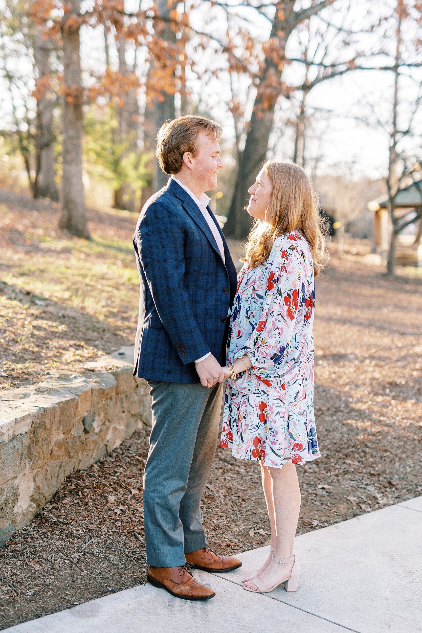 couple holds hands in front of stone wall during engagement portraits in Independence Park in Charlotte NC