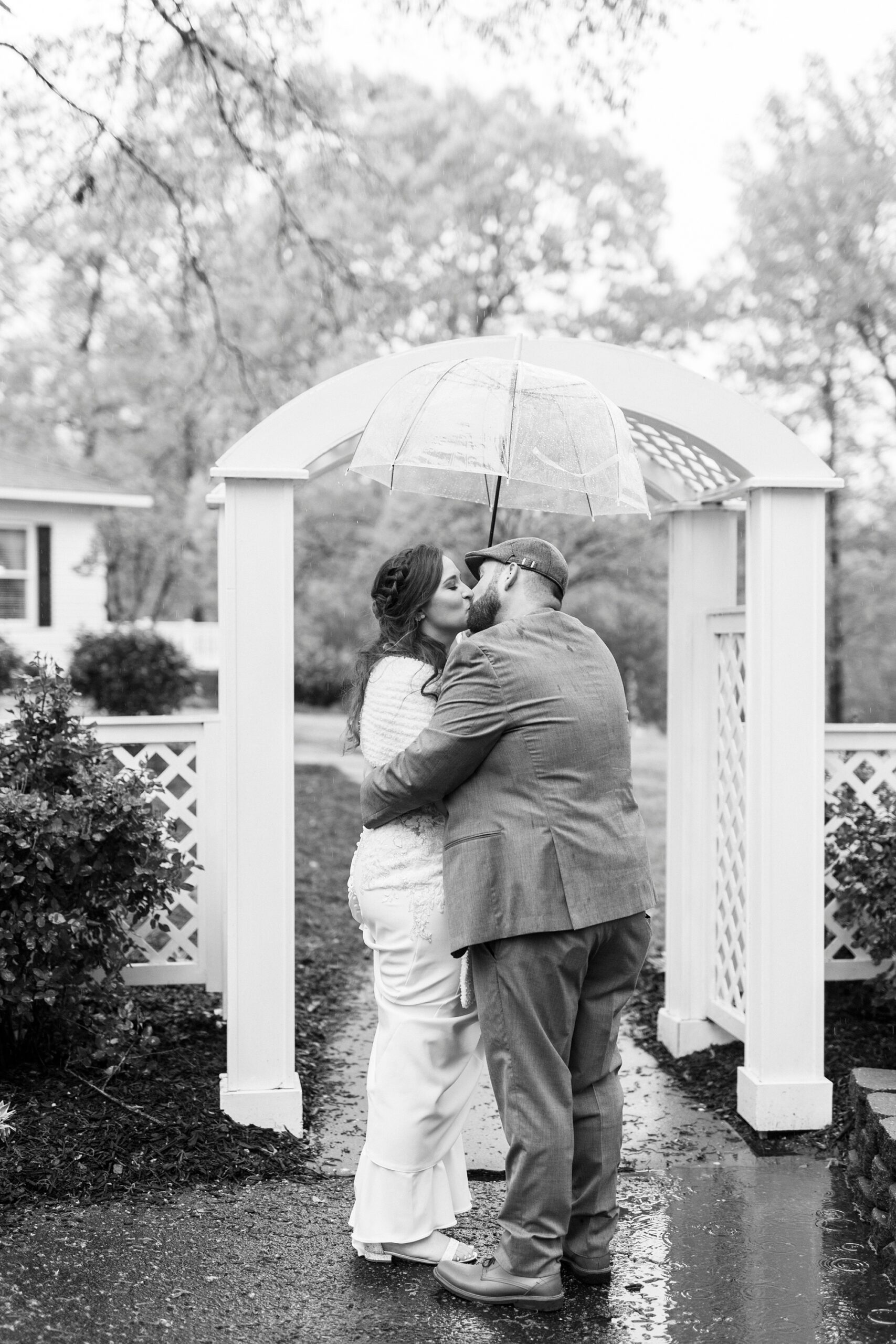 bride and groom kiss under umbrellas by white arbor on rainy day 