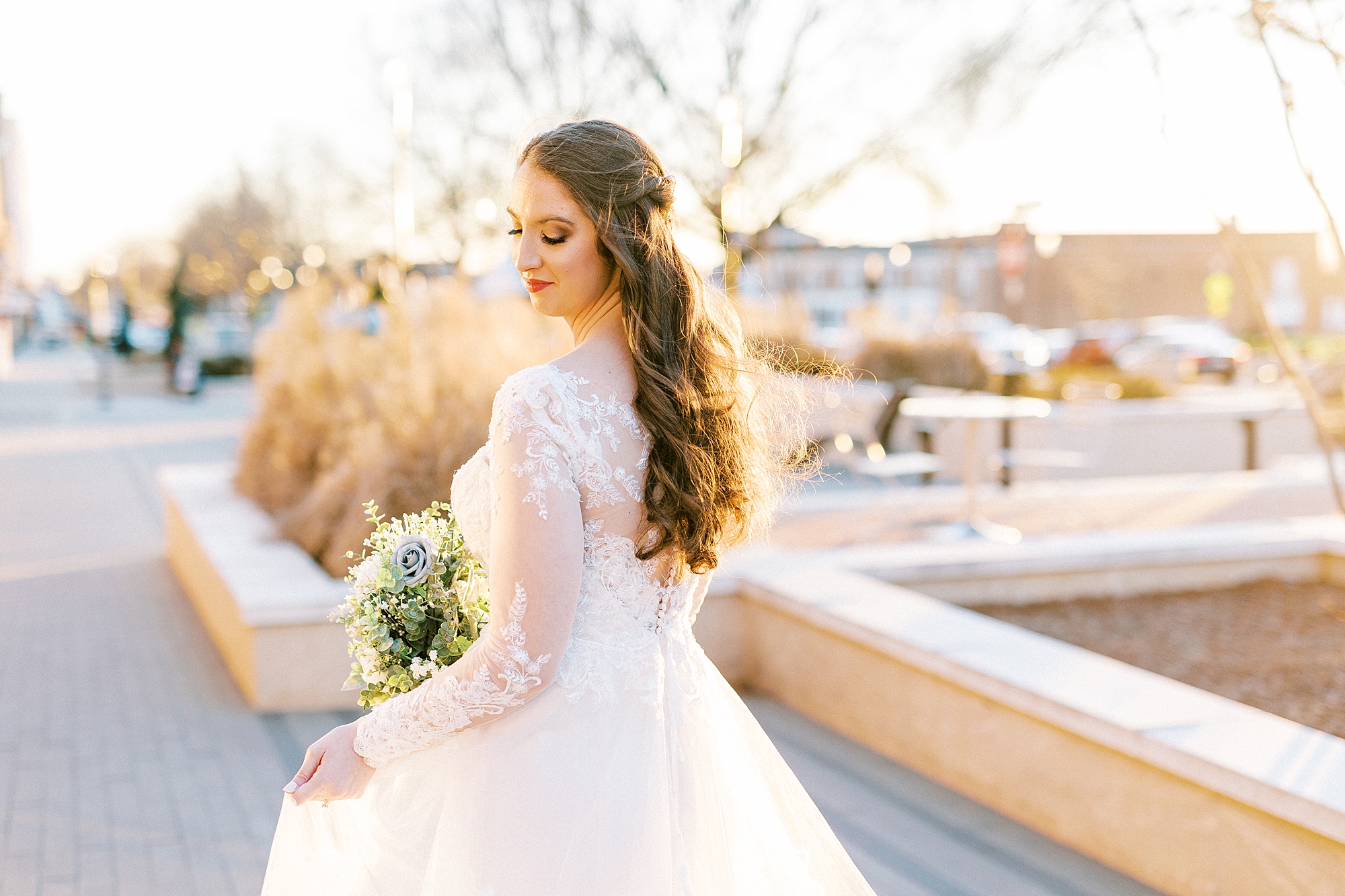 bride in long sleeve wedding dress holds skirt and looks over shoulder 