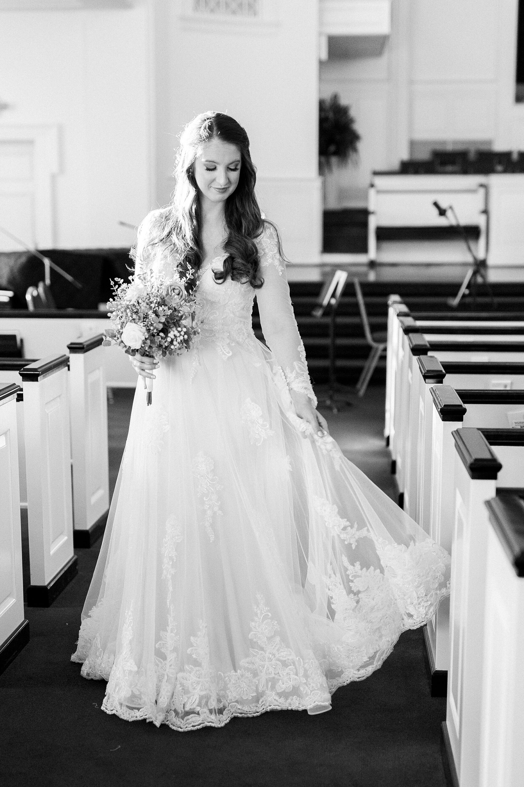 bride stands in aisle of church in Downtown Kannapolis holding skirt of gown 