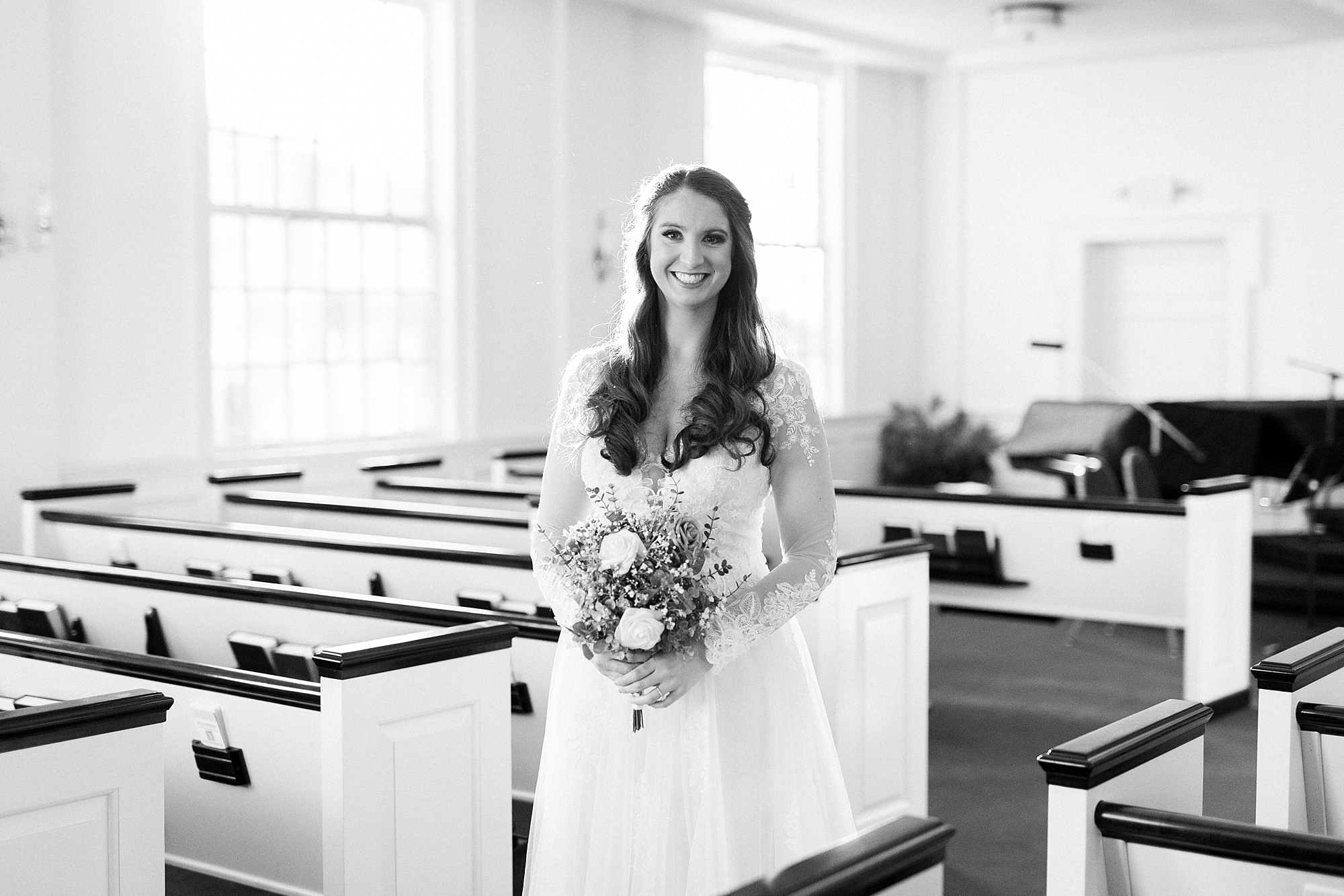 bride smiles in aisle of Downtown Kannapolis church holding white bouquet 