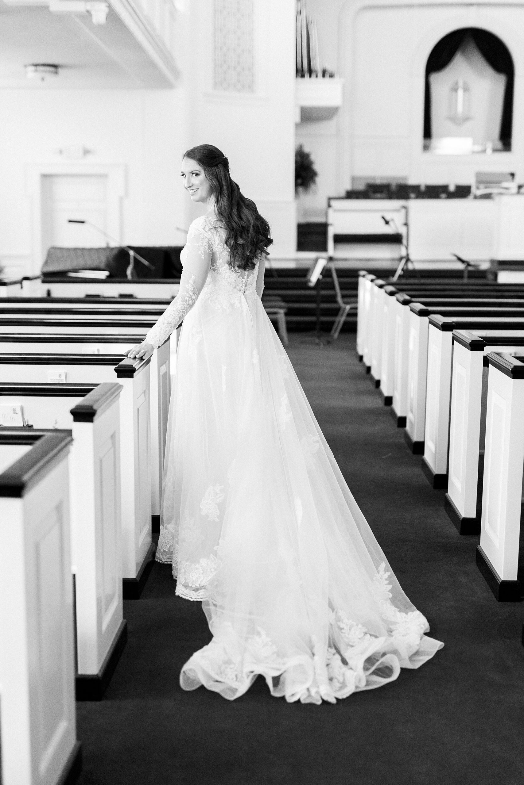 bride holds pew in aisle of church in Downtown Kannapolis
