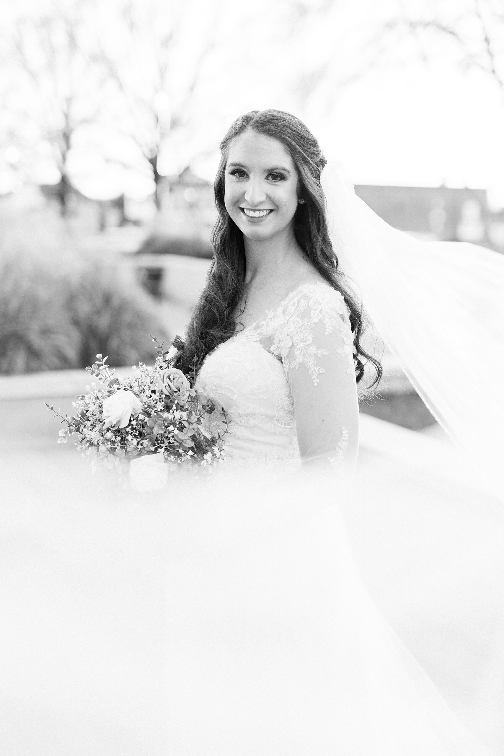bride smiles with veil floating around her outside building in Downtown Kannapolis