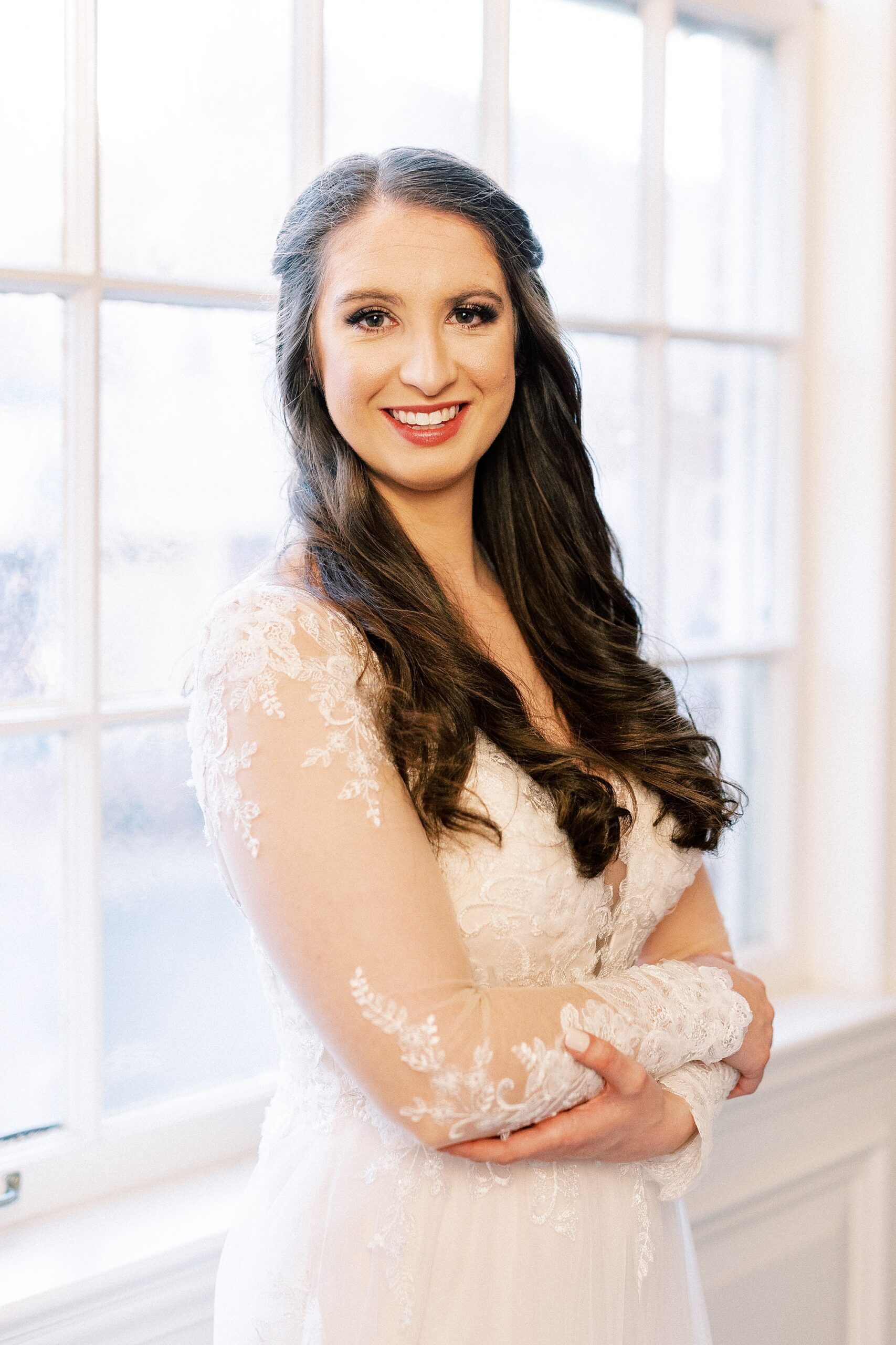bride grins with arms crossed in lace sleeves of wedding gown during southern bridal portraits 