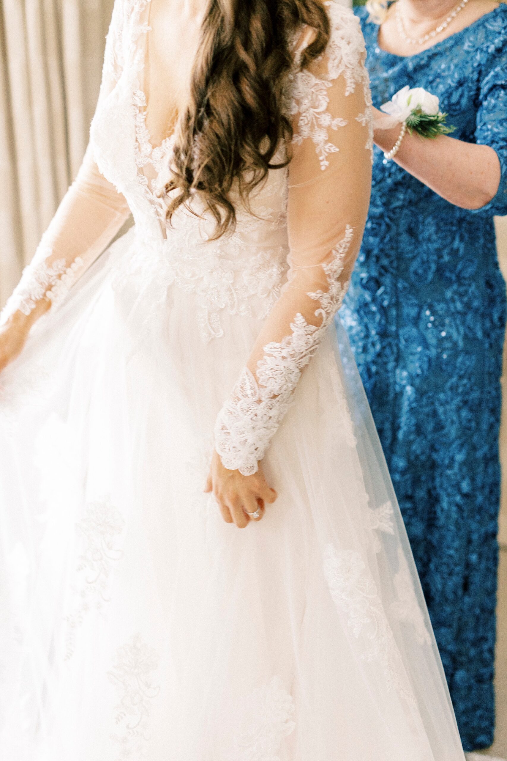 mother in blue dress helps bride with buttons on gown