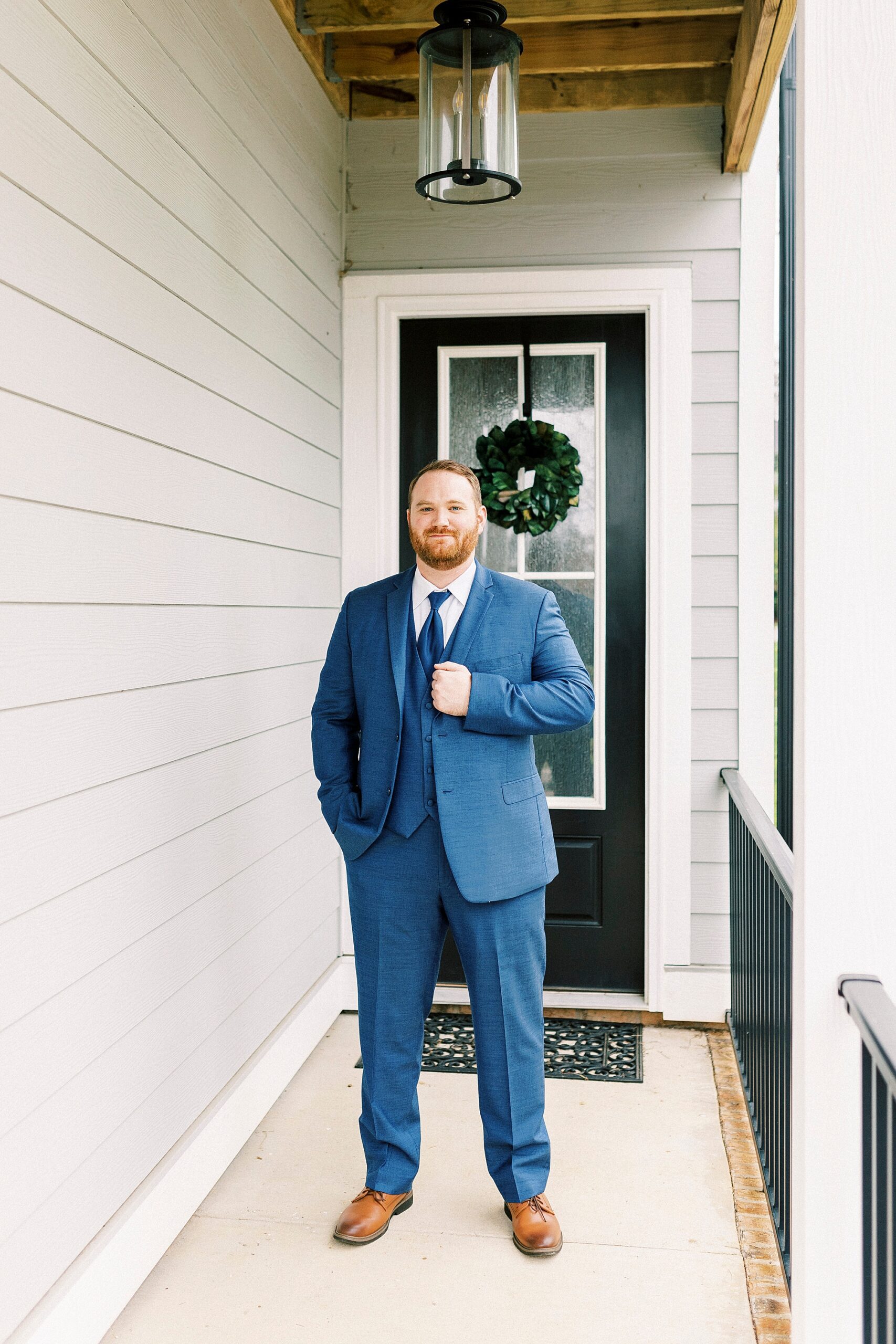 groom in blue suit stands outside front door holding lapel