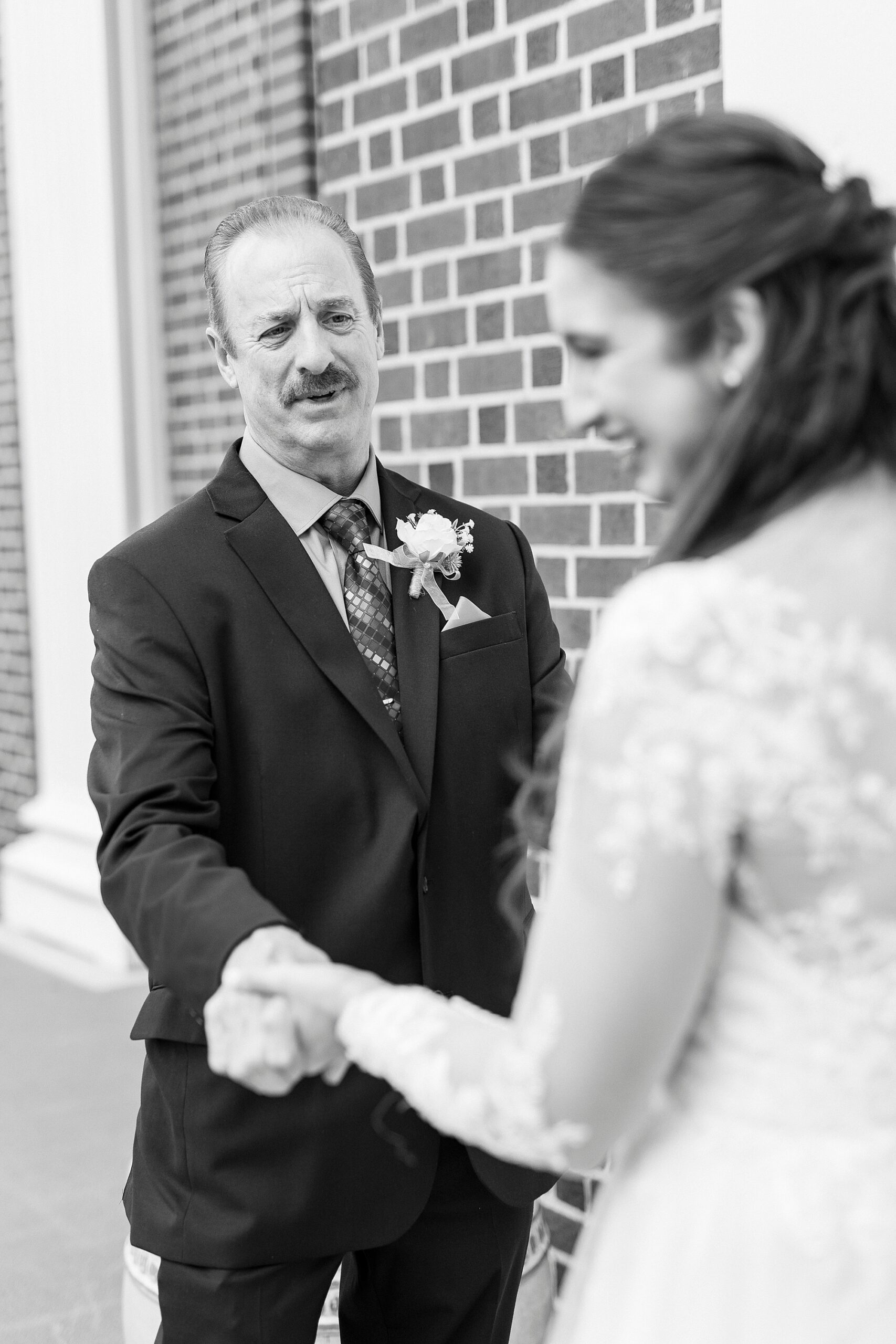 bride and father hold hands during first look outside First Baptist Church in Kannapolis NC