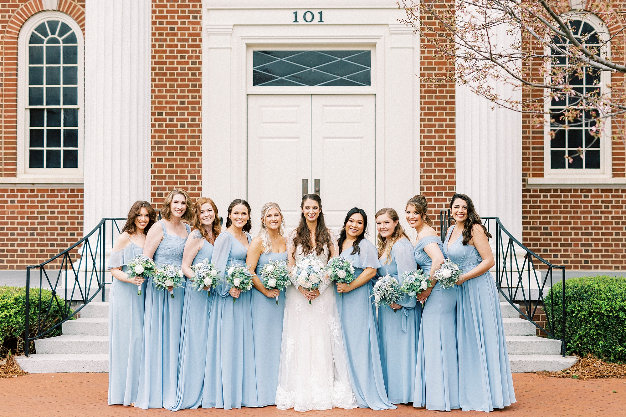 bride stands with bridesmaids in light bleu gowns on steps of First Baptist Church in Kannapolis NC