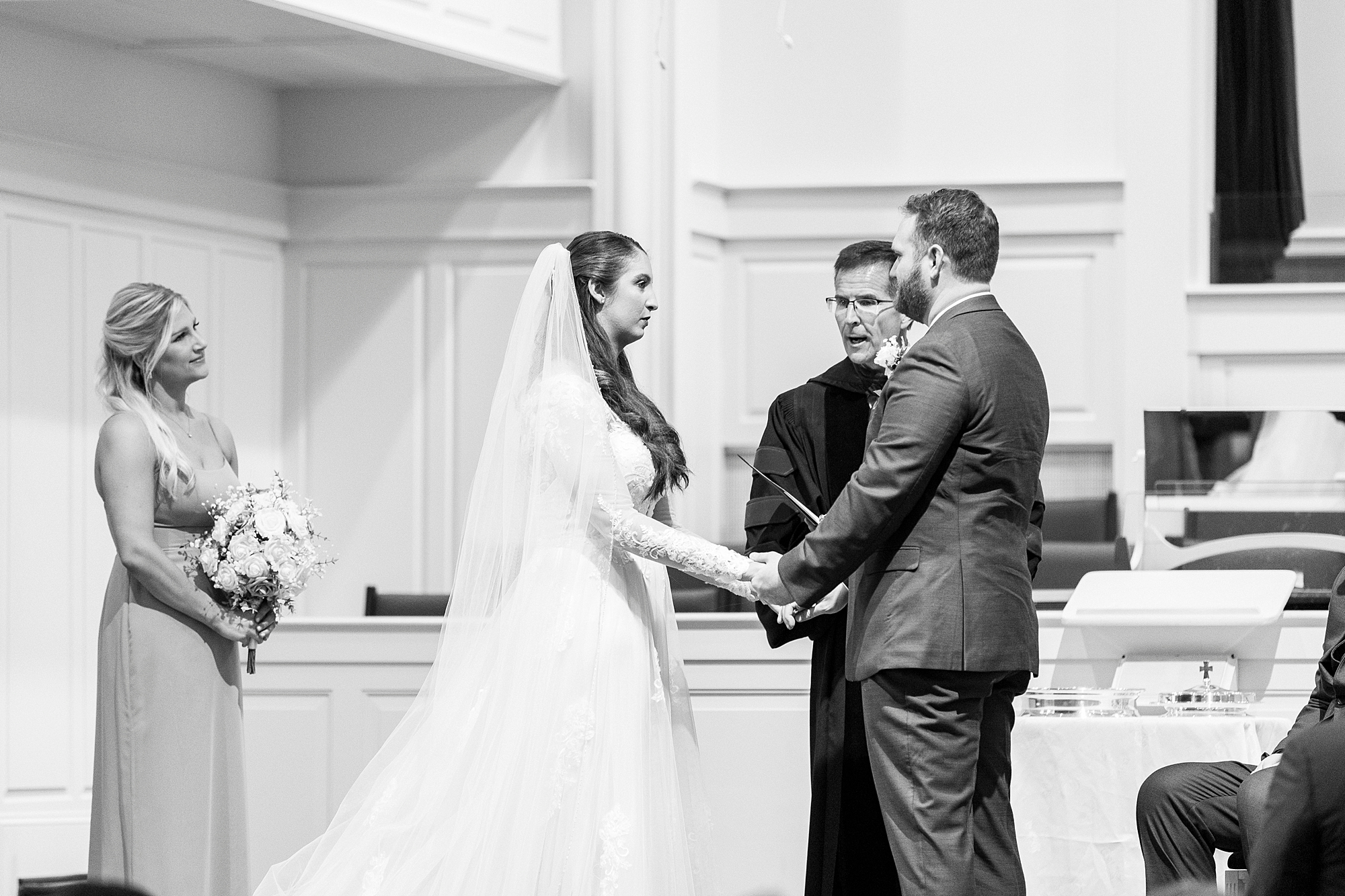 newlyweds hold hands during ceremony inside First Baptist Church in Kannapolis NC
