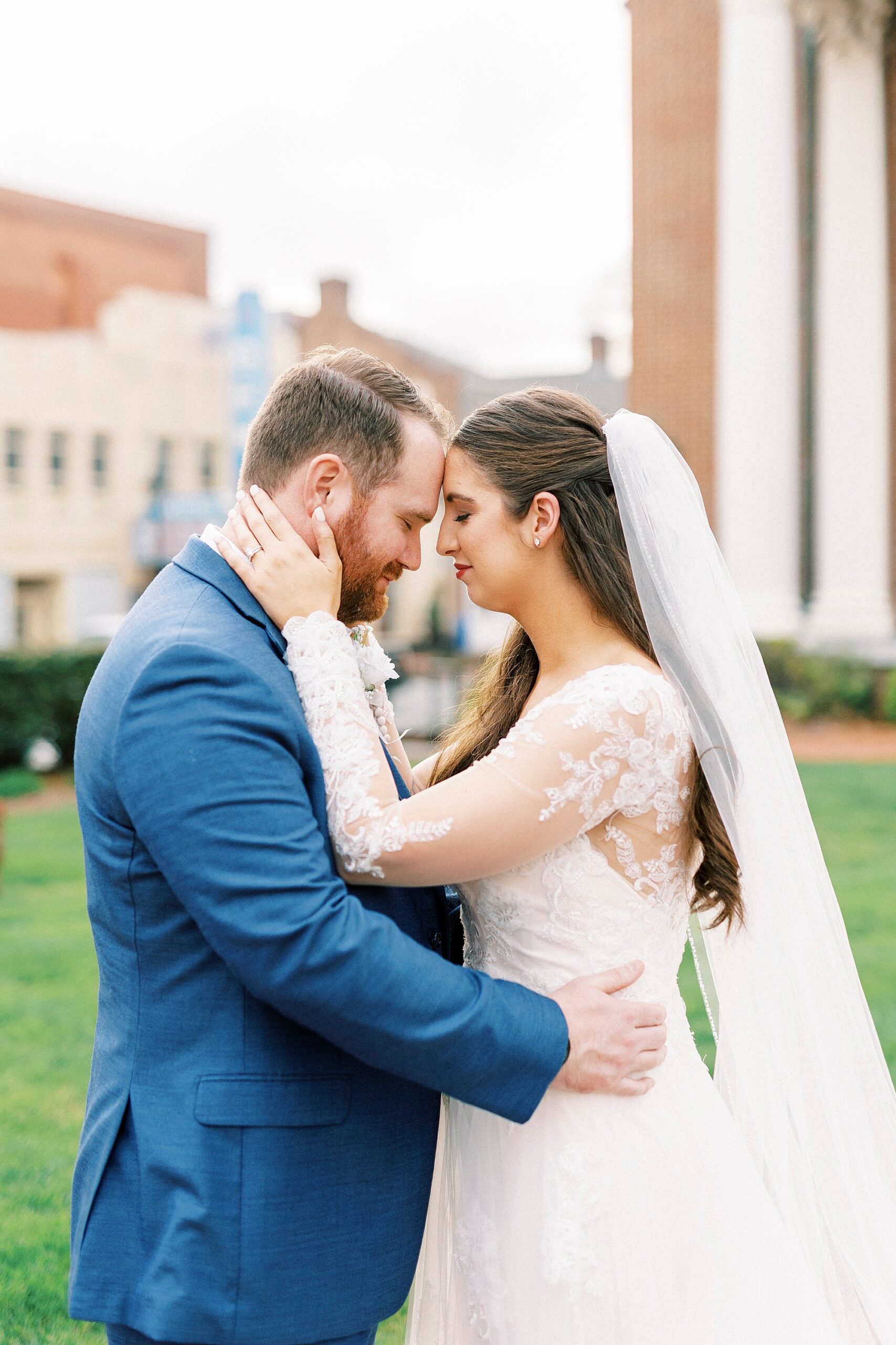 bride and groom hug leaning heads together outside church in Downtown Kannapolis