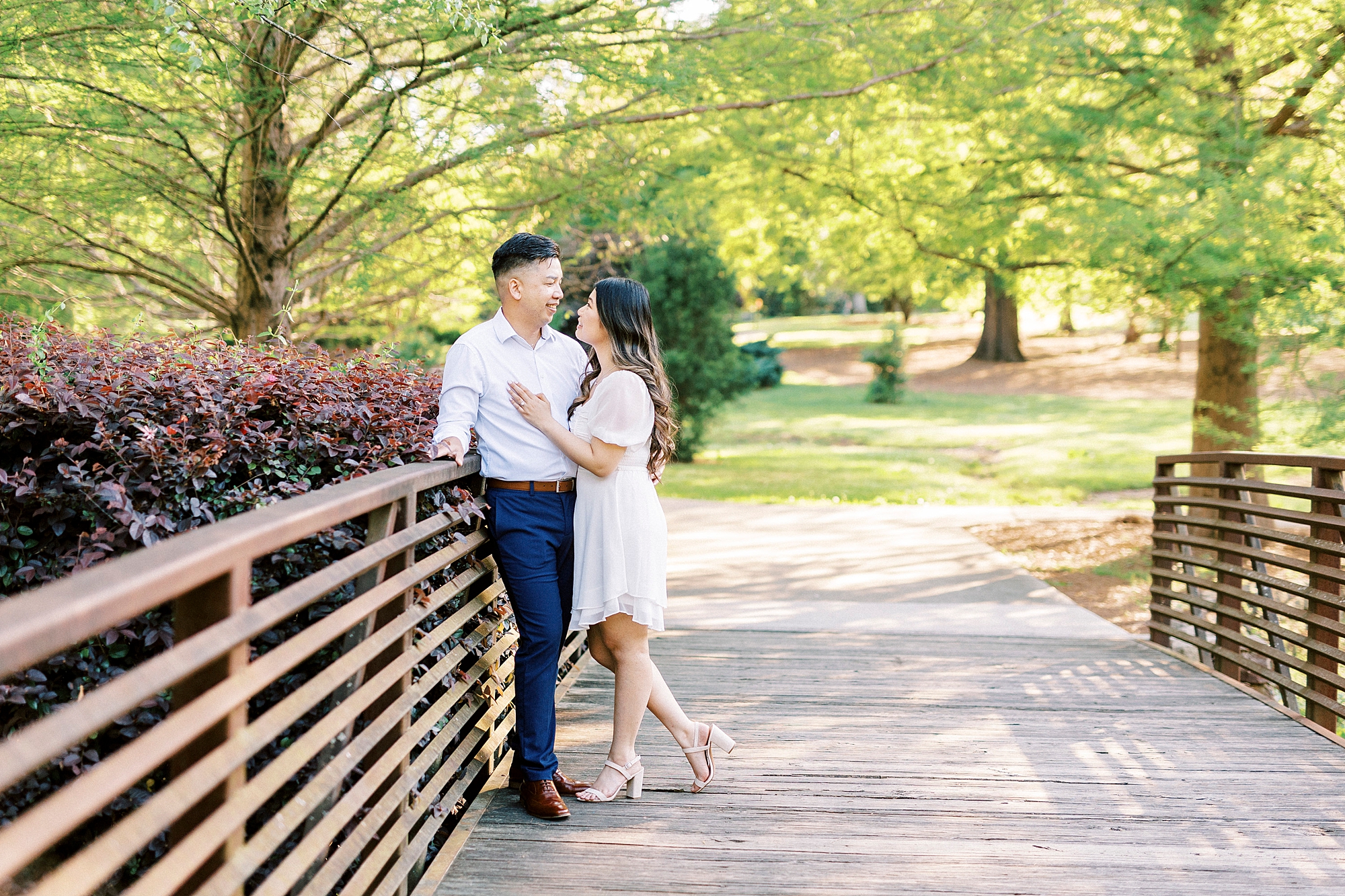 woman in white dress leans against man standing on wooden bridge in Glencairn Garden 