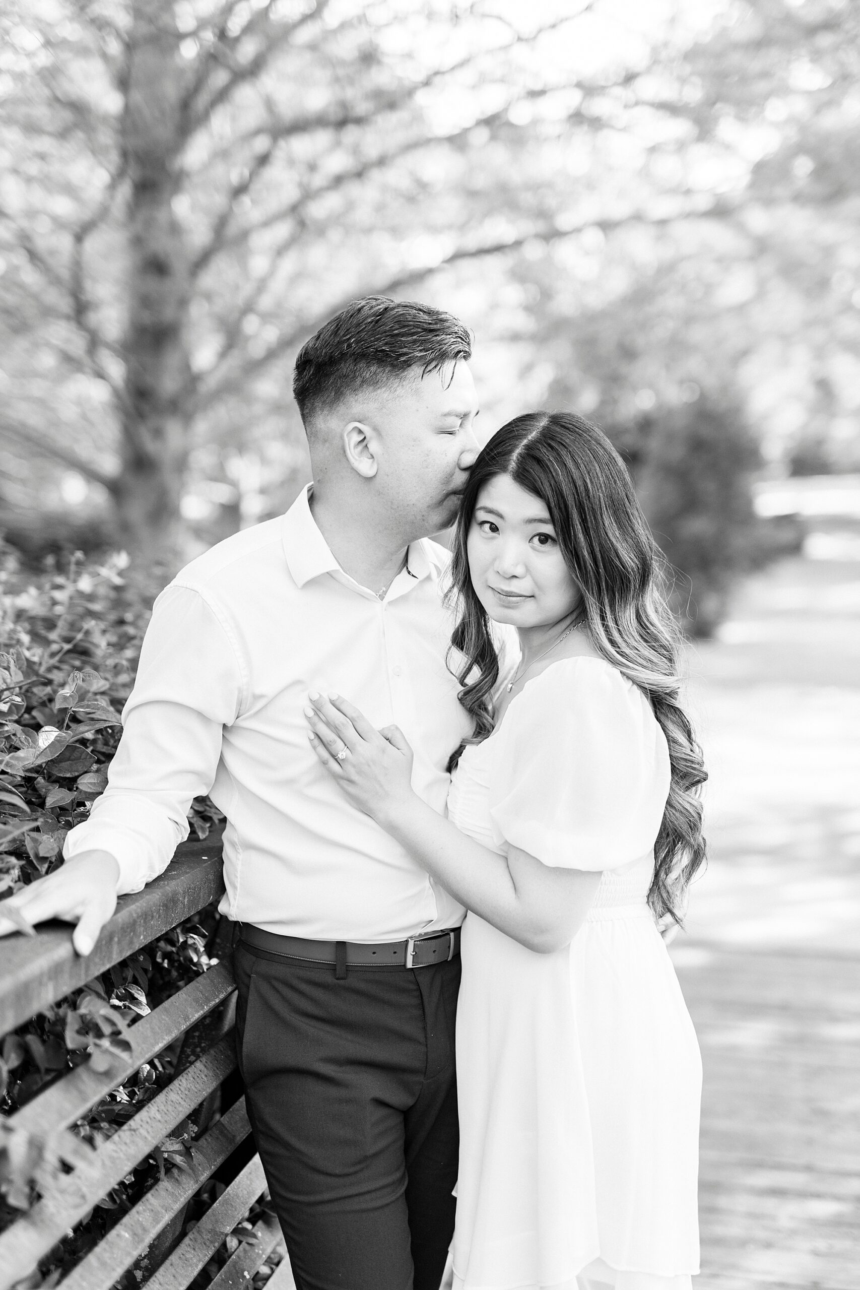 man leans to whisper in woman's ear hugging against wooden railing 