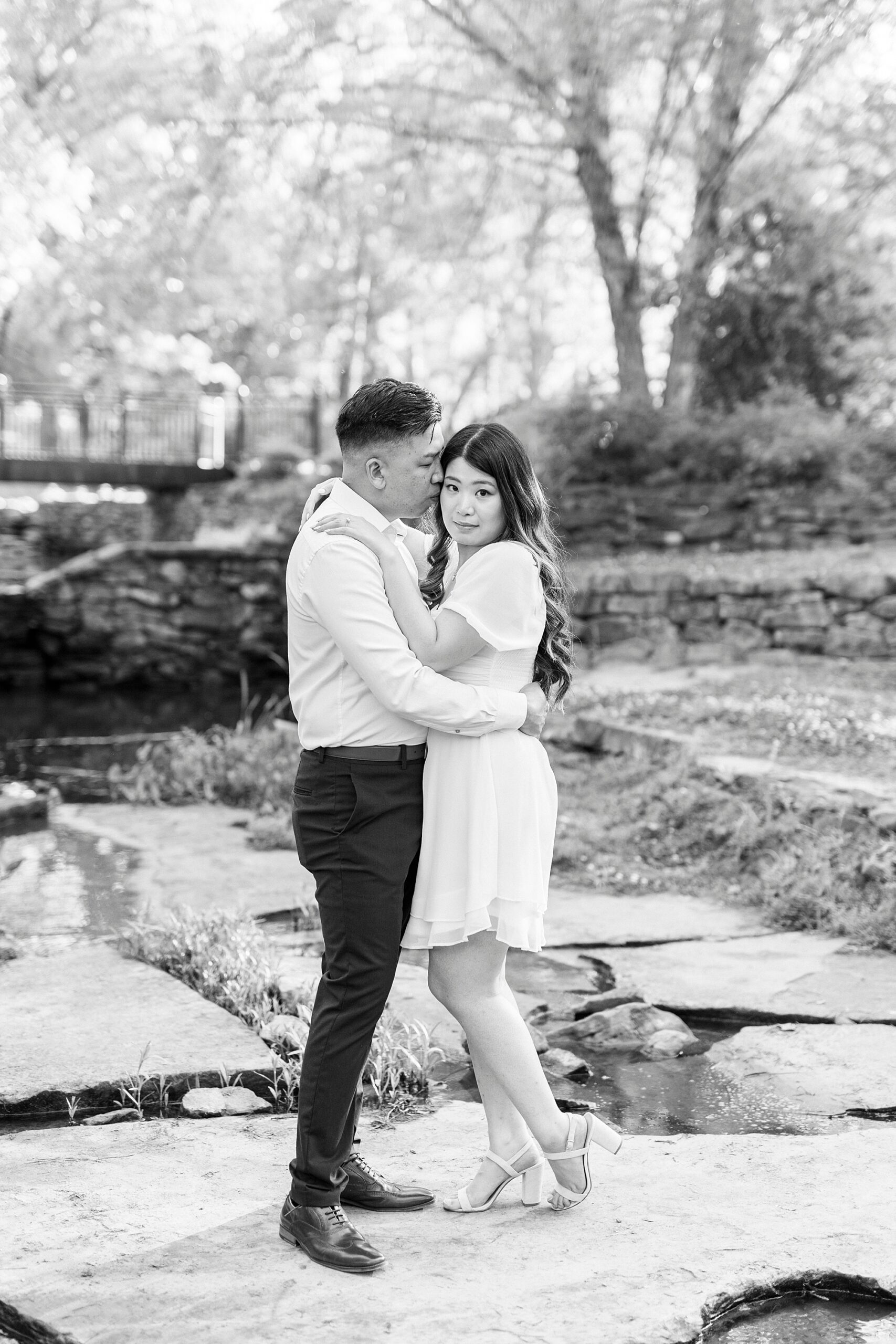 engaged couple hugs on rocks in the pond at Glencairn Garden