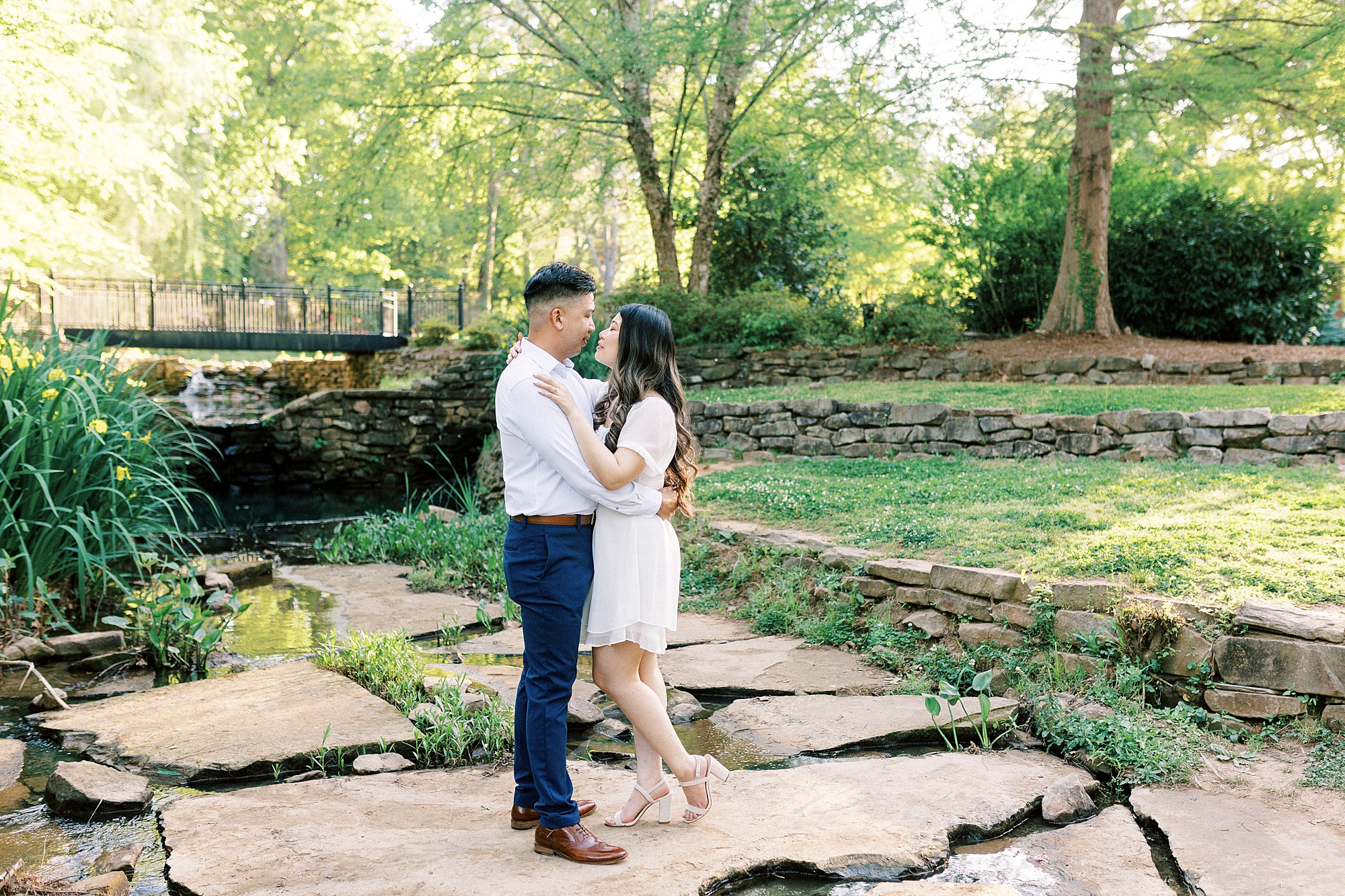 engaged couple stands on stones in the pond at Glencairn Garden